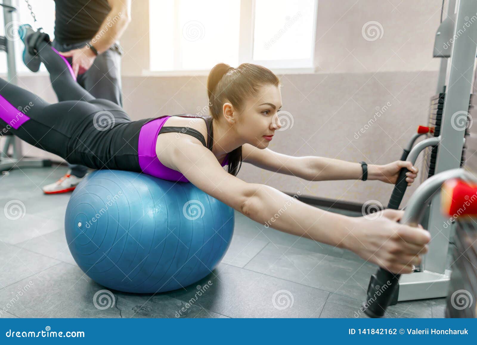 young woman doing rehabilitation exercises with personal instructor using kinesi machine, fitness gym background. kinesis