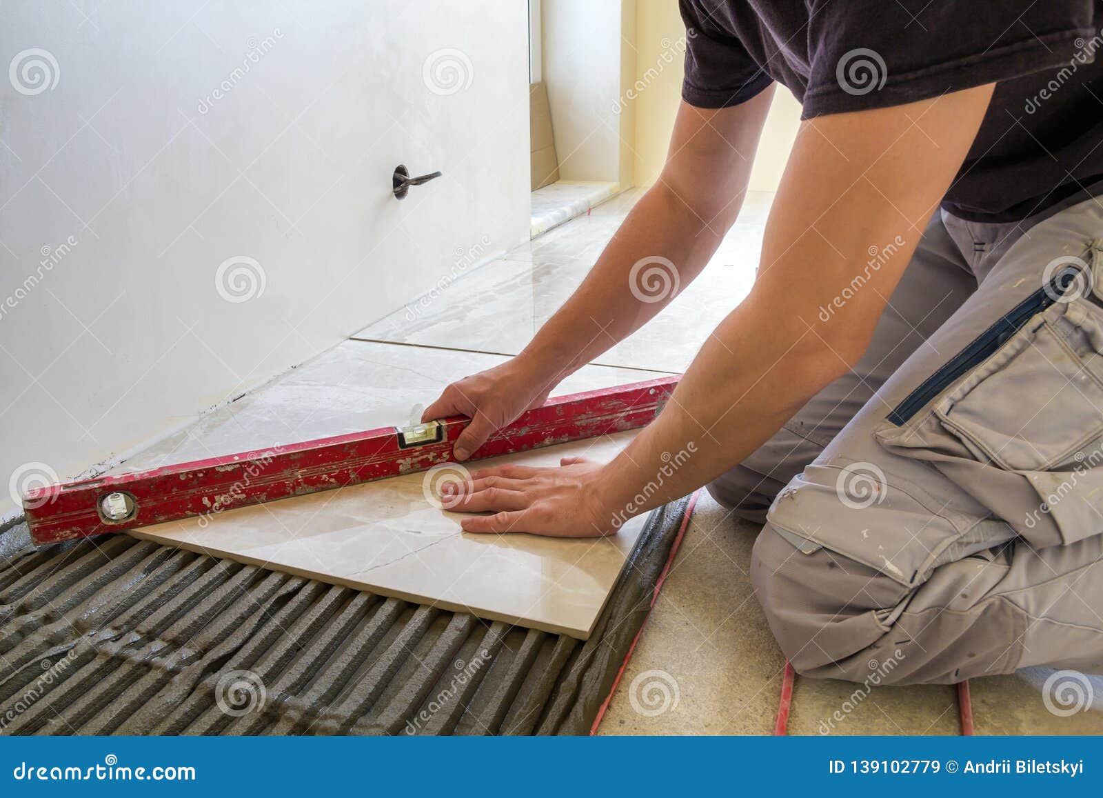 Young Worker Tiler Installing Ceramic Tiles Using Lever On Cement