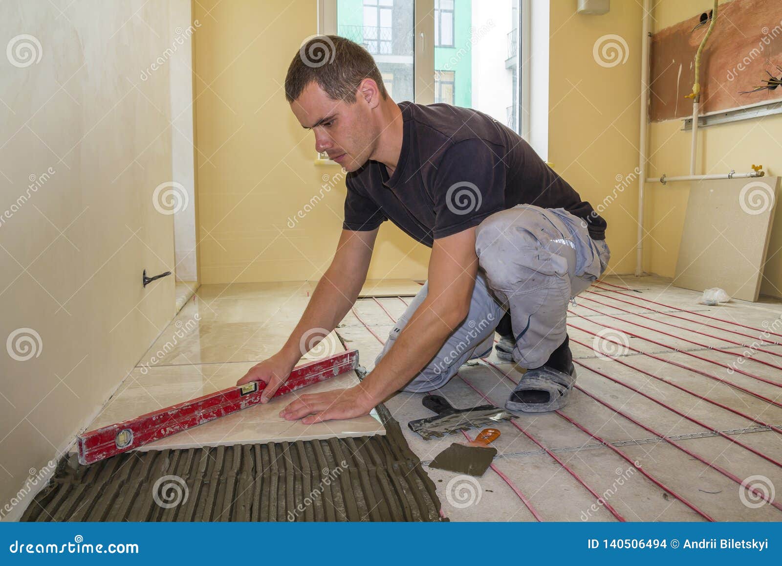 Young Worker Tiler Installing Ceramic Tiles Using Lever On Cement