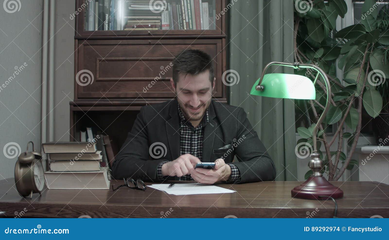 Young Writer At His Desk Happily Messaging On Mobile Phone Stock