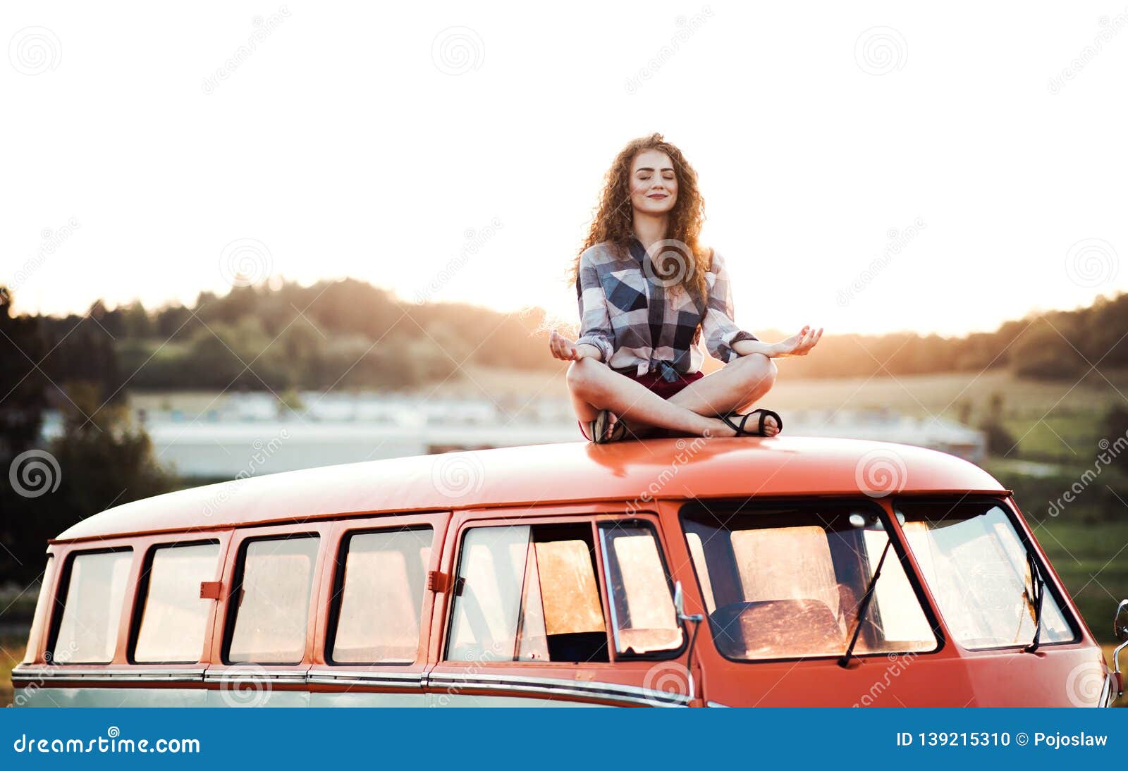 a young girl on a roadtrip through countryside, sitting on the roof of minivan doing yoga.