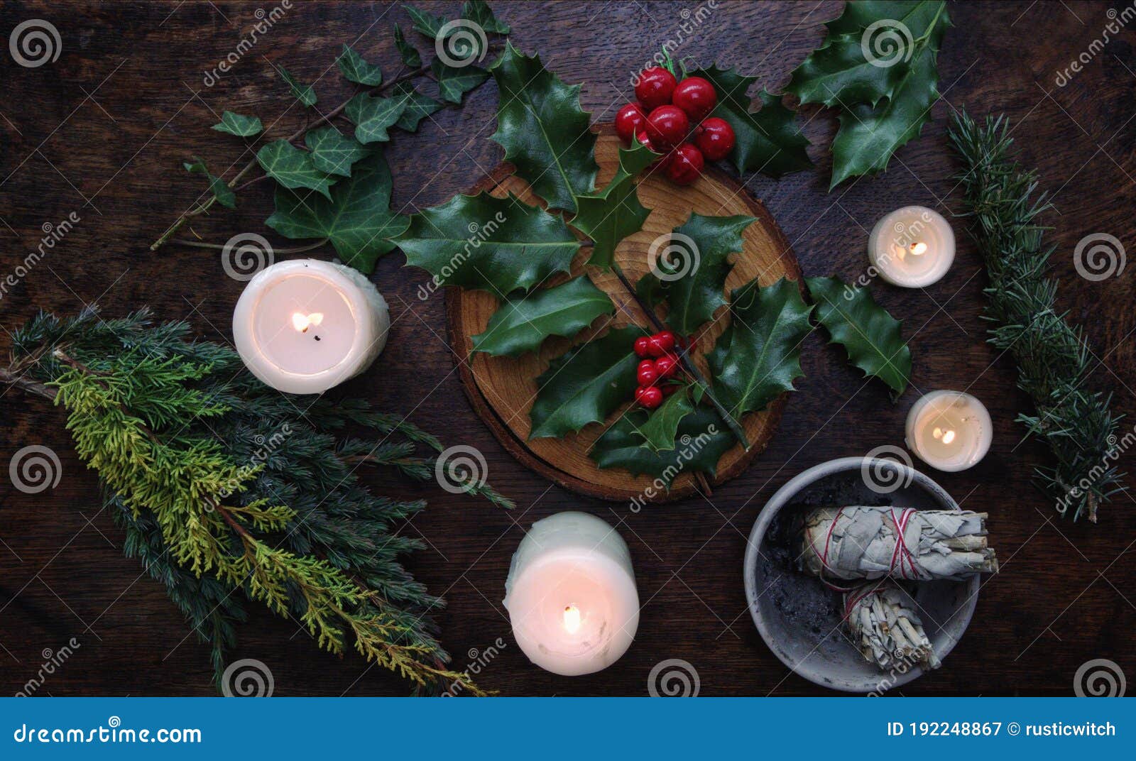 yule winter solstice christmas themed flat lay with branch of holly plant on a dark wooden table