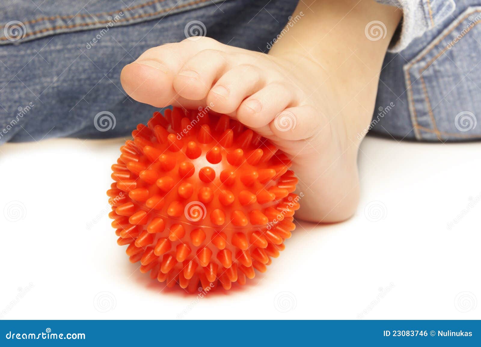 Z masaż plastikową piłką dziecko stopa. Dziecka stopa z tło plastikową pomarańczową masażu piłką na biały tle