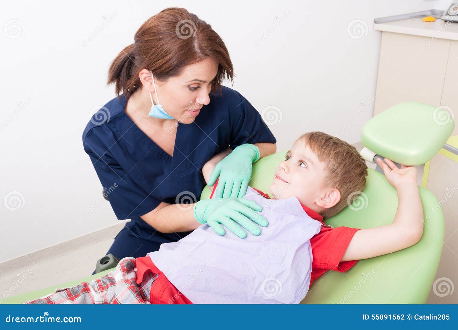Zahnarztfrau, die mit Kinderpatienten spricht. Zahnarztfrauen, die mit Kinderpatienten sprechen, der im glücklichen Zahnarztstuhl sitzt