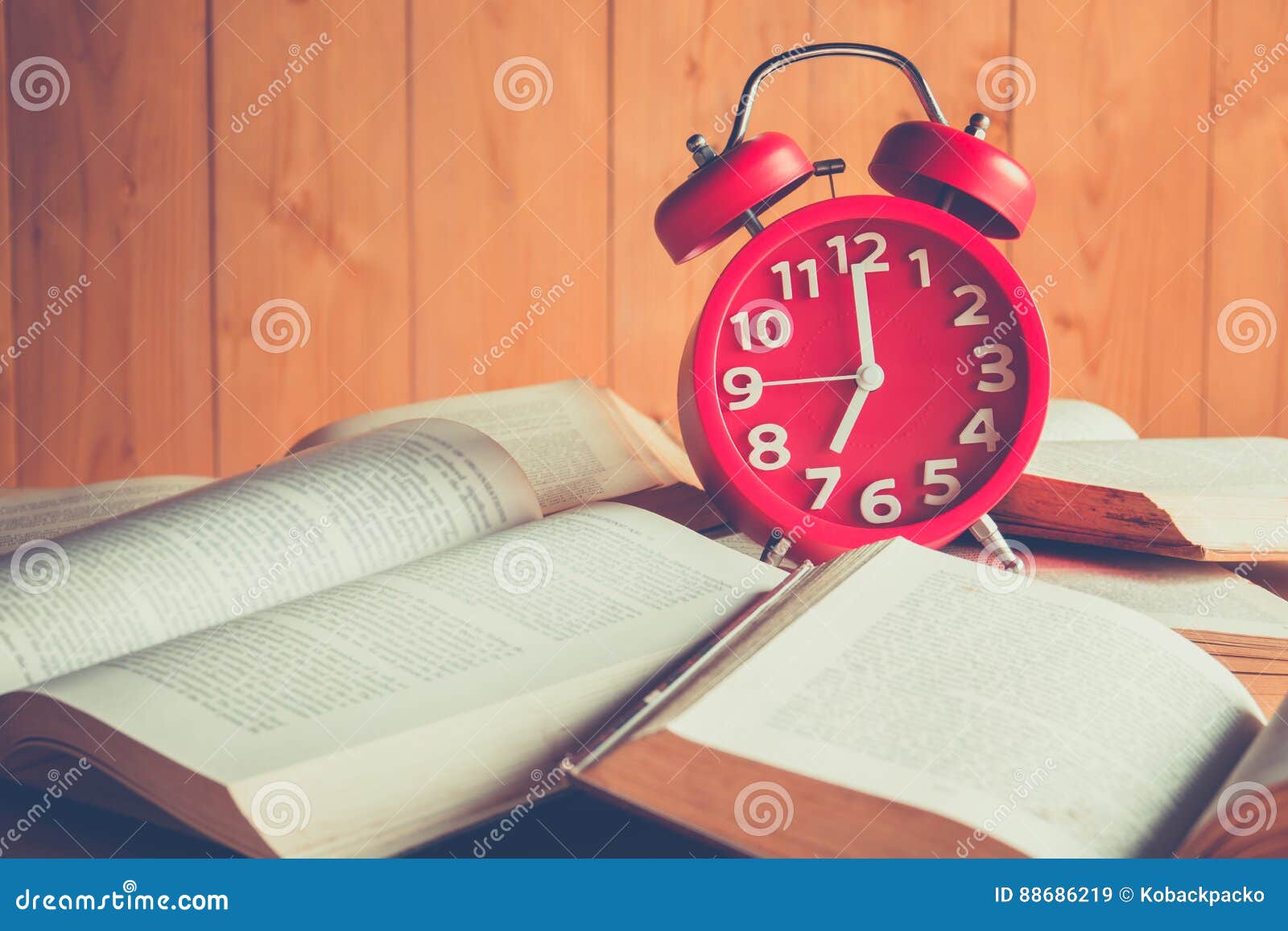 Zegar i książka. Czerwony budzik na stert starych książkach