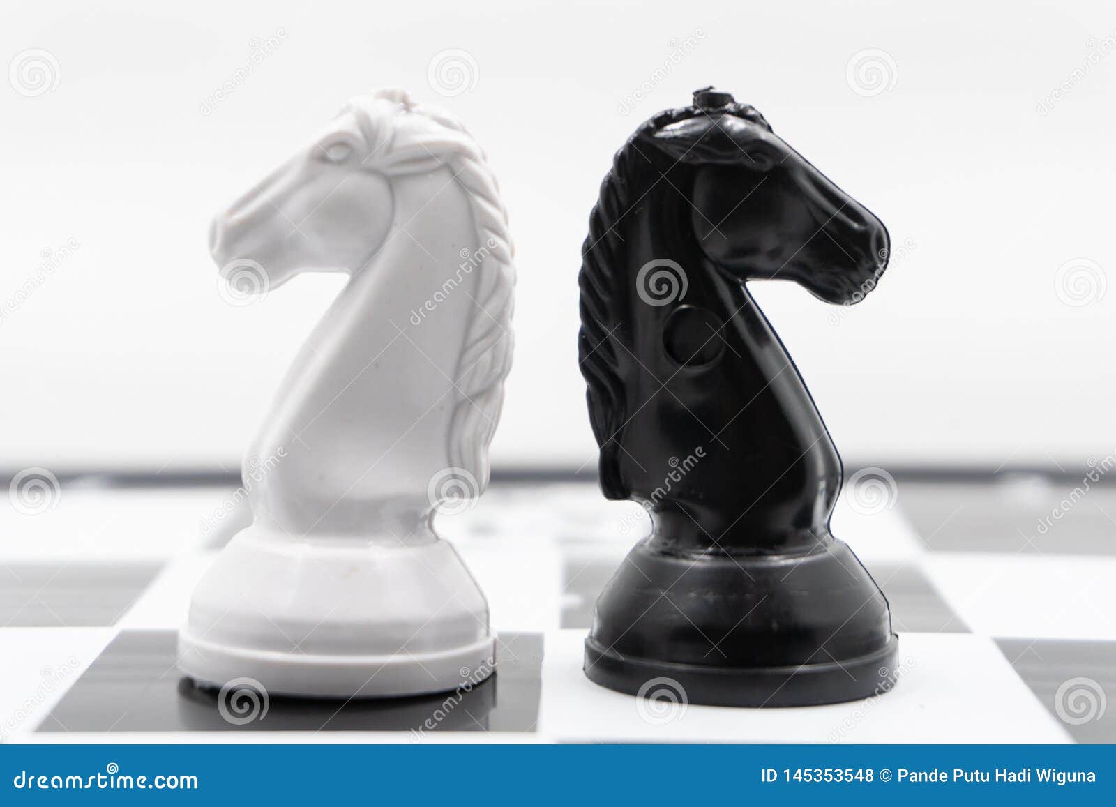 Two chess knights turned back to each other. There is a white background for placing posts. two chess knights, black and white, turned back to each other. There is a white background for placing posts