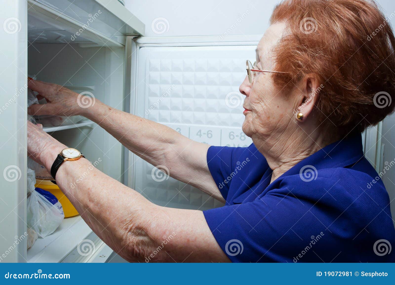 Ältere Frau, die nach Nahrung im Kühlraum sucht. Erwachsene Frauen, die ihre Nahrung in der Gefriermaschine für das Kochen suchen