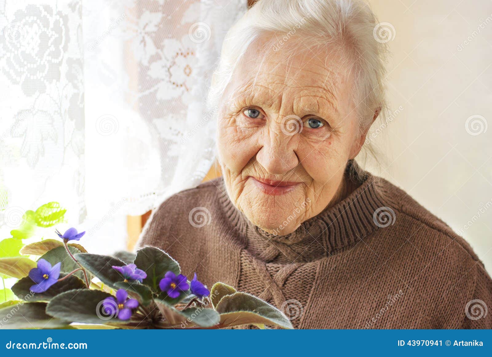 Ältere Frauenblume. Porträt ofa lächelnde ältere Frau mit Blume zu Hause