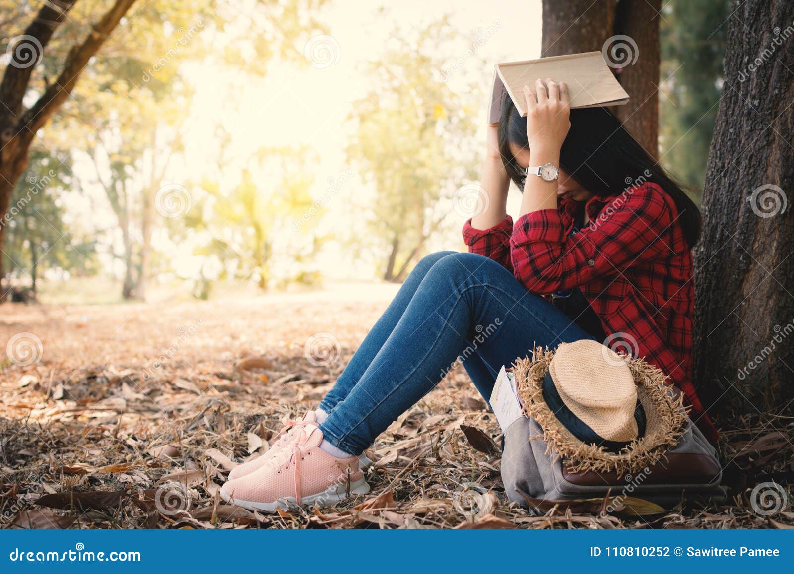 Ångestkvinnan om henne som studerar att sitta som är ensamt under det stora trädet parkerar på, färg av tappningsignalen och den mjuka fokusen