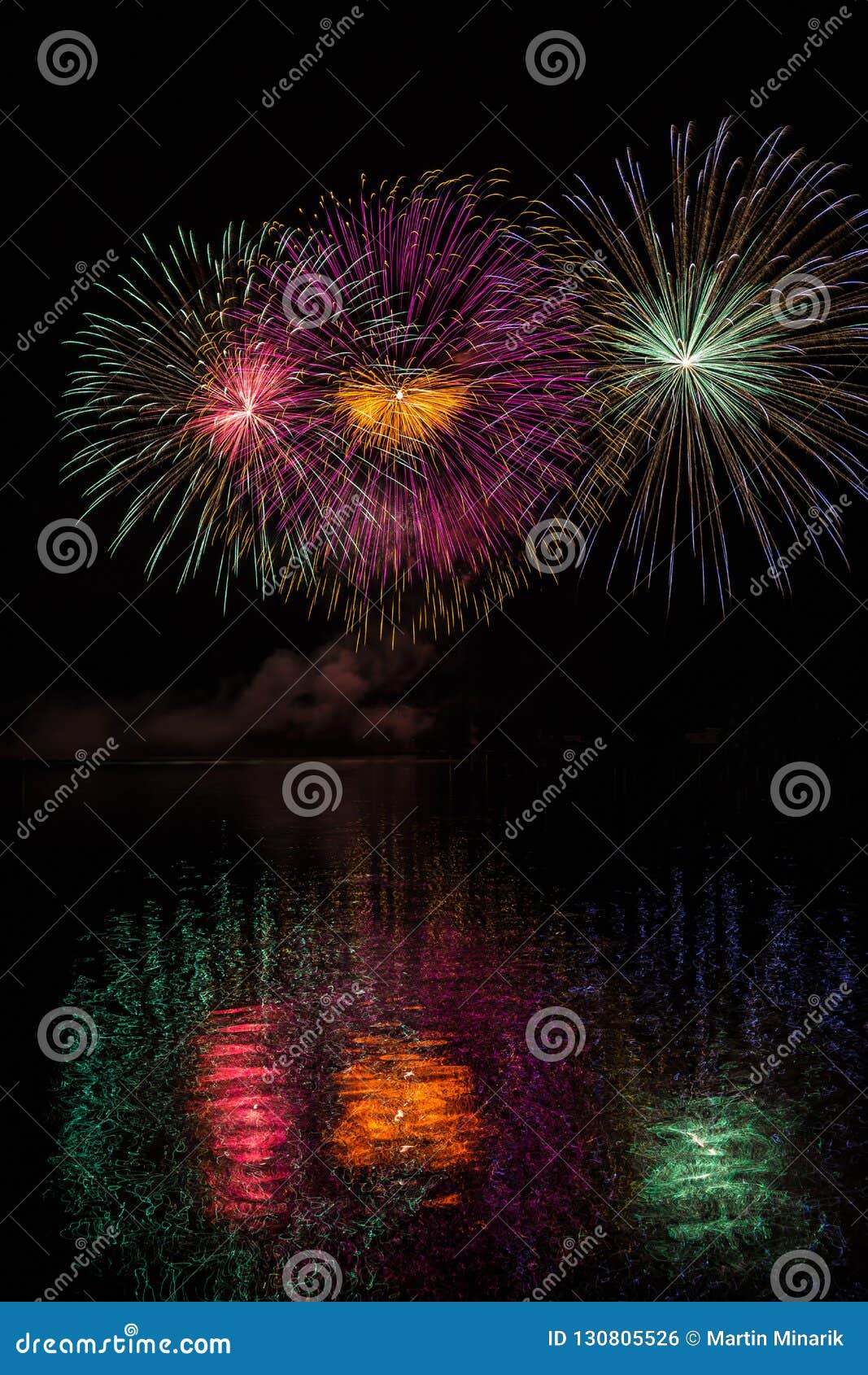Étoiles multicolores énormes dans des feux d'artifice au-dessus de la surface du barrage de Brno avec la réflexion de lac