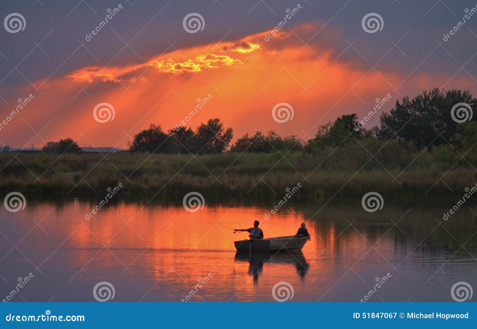 Łowić na spokojnym wieczór. Dwa rybaka w łódkowatym połowie jako słońce ustawiają