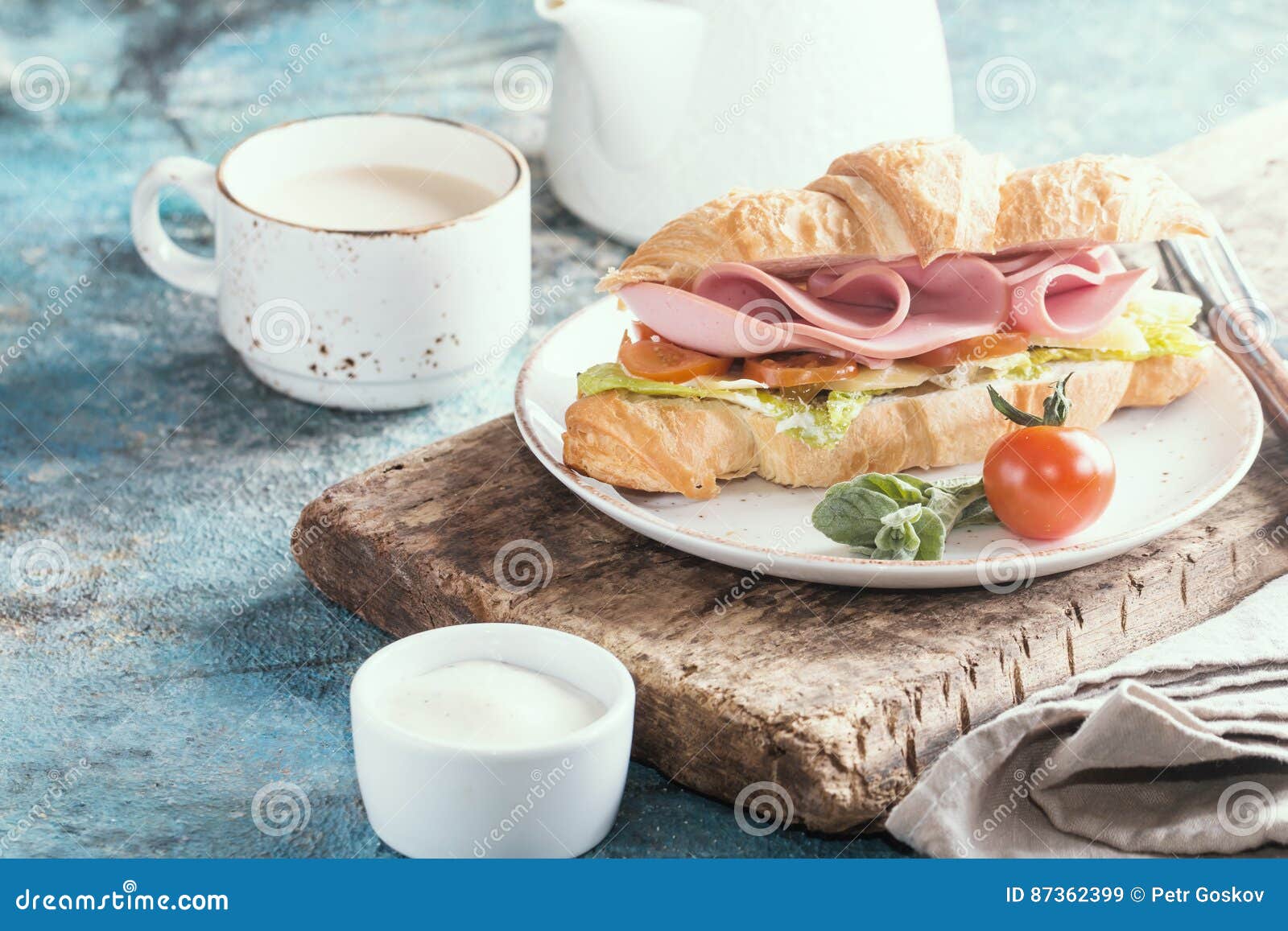 Świeża croissant kanapka z baleronem, ser i sałatka, leaf z kawą na błękita stole