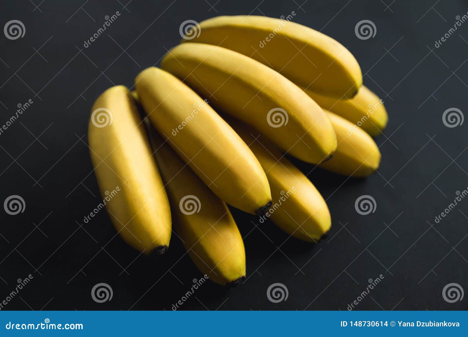 Yellow bright ripe bananas lie on a black background. Delicious banana branch. Fruit on a black background.