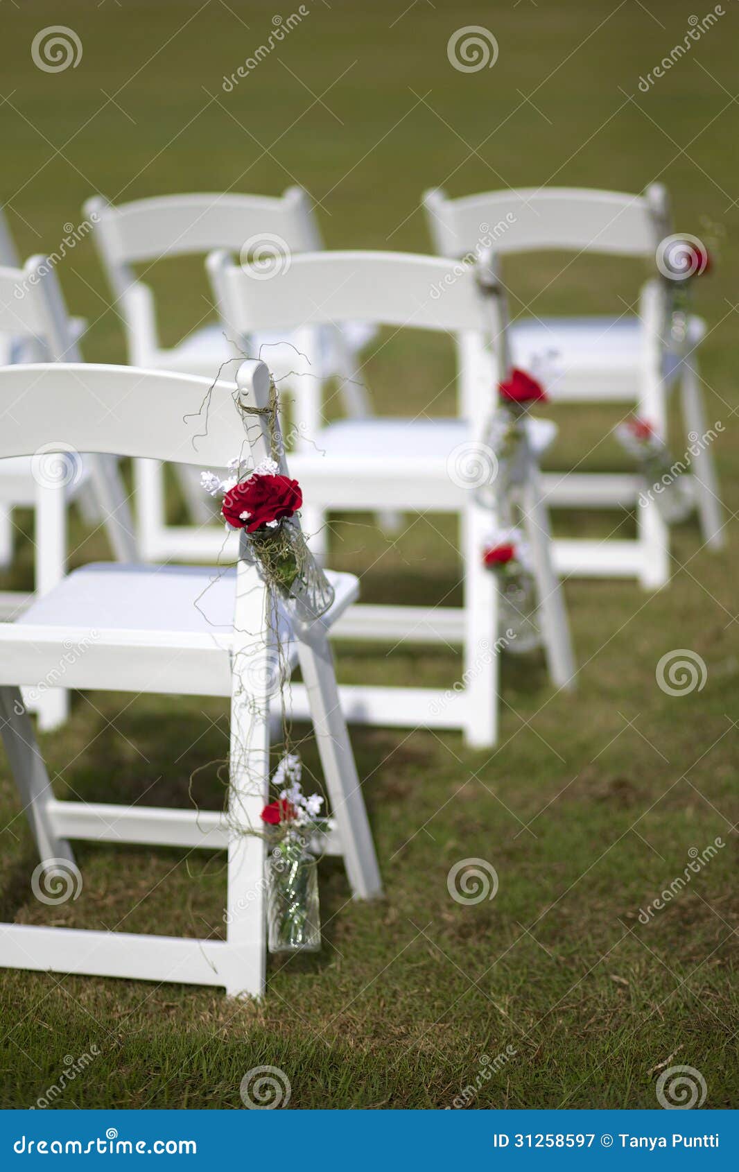 Άσπρες γαμήλιες καρέκλες με τις ροδαλές διακοσμήσεις που κρεμούν στην πλευρά.