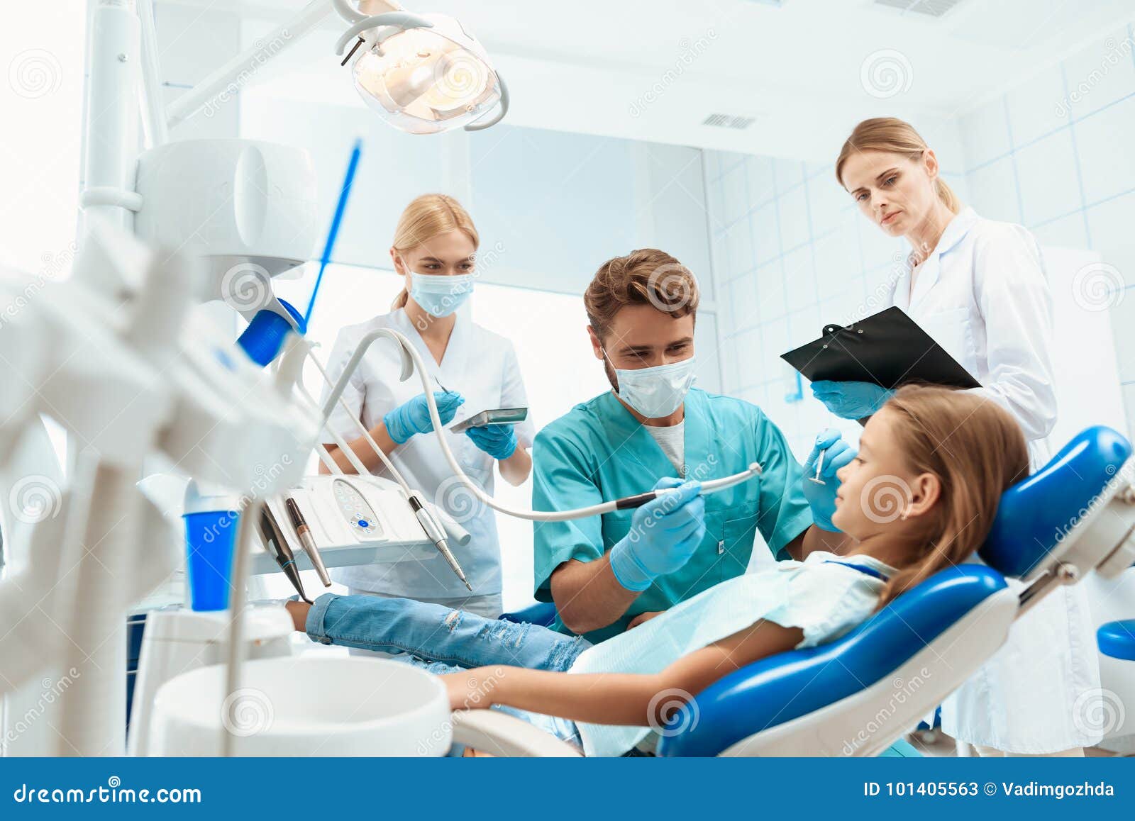 Ένας οδοντίατρος προετοιμάζεται να μεταχειριστεί τα δόντια ενός μικρού κοριτσιού Υπάρχουν νοσοκόμες γύρω απομονωμένο κορίτσι λευκ. Ένα μικρό κορίτσι κάθεται σε μια πολυθρόνα σε μια υποδοχή με έναν που οδοντίατρο ο οδοντίατρος ήταν έτοιμος να θεραπεύσει το κορίτσι Γύρω από τους είναι νοσοκόμες