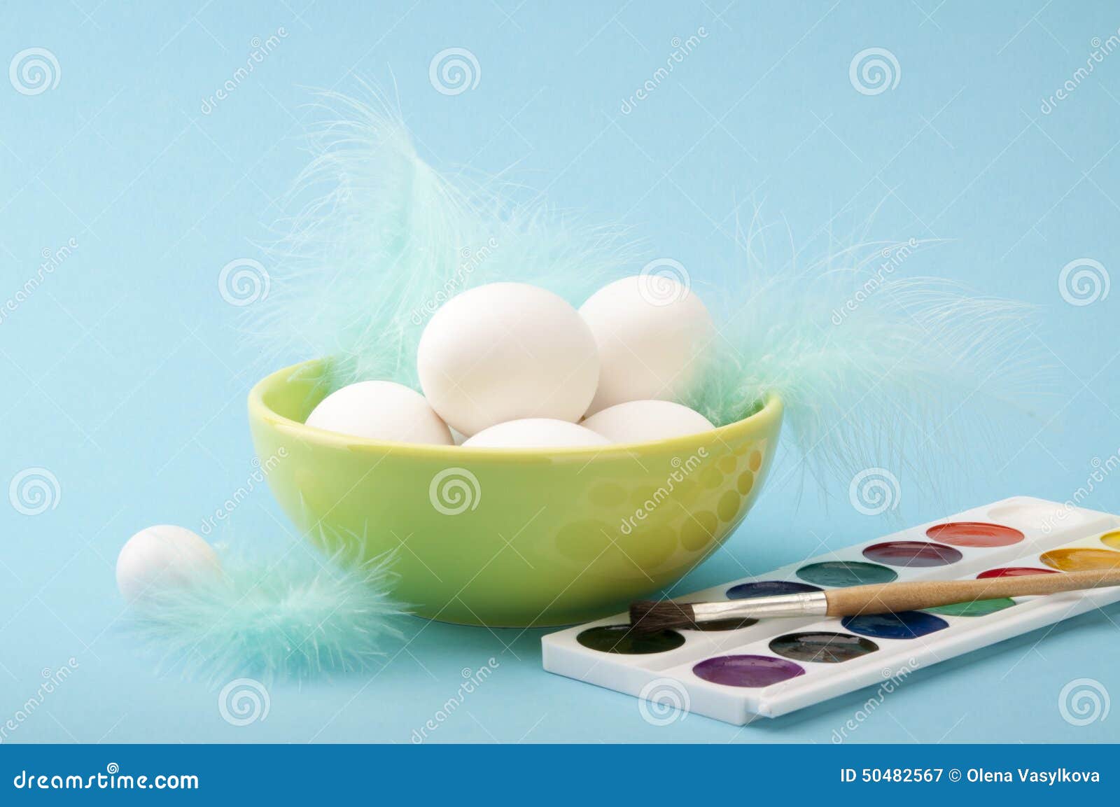 Αυγά Πάσχας. Το Watercolors με τη ζωγραφική βουρτσίζουν και τα αυγά Πάσχας στο κύπελλο με τα φτερά στο μπλε υπόβαθρο