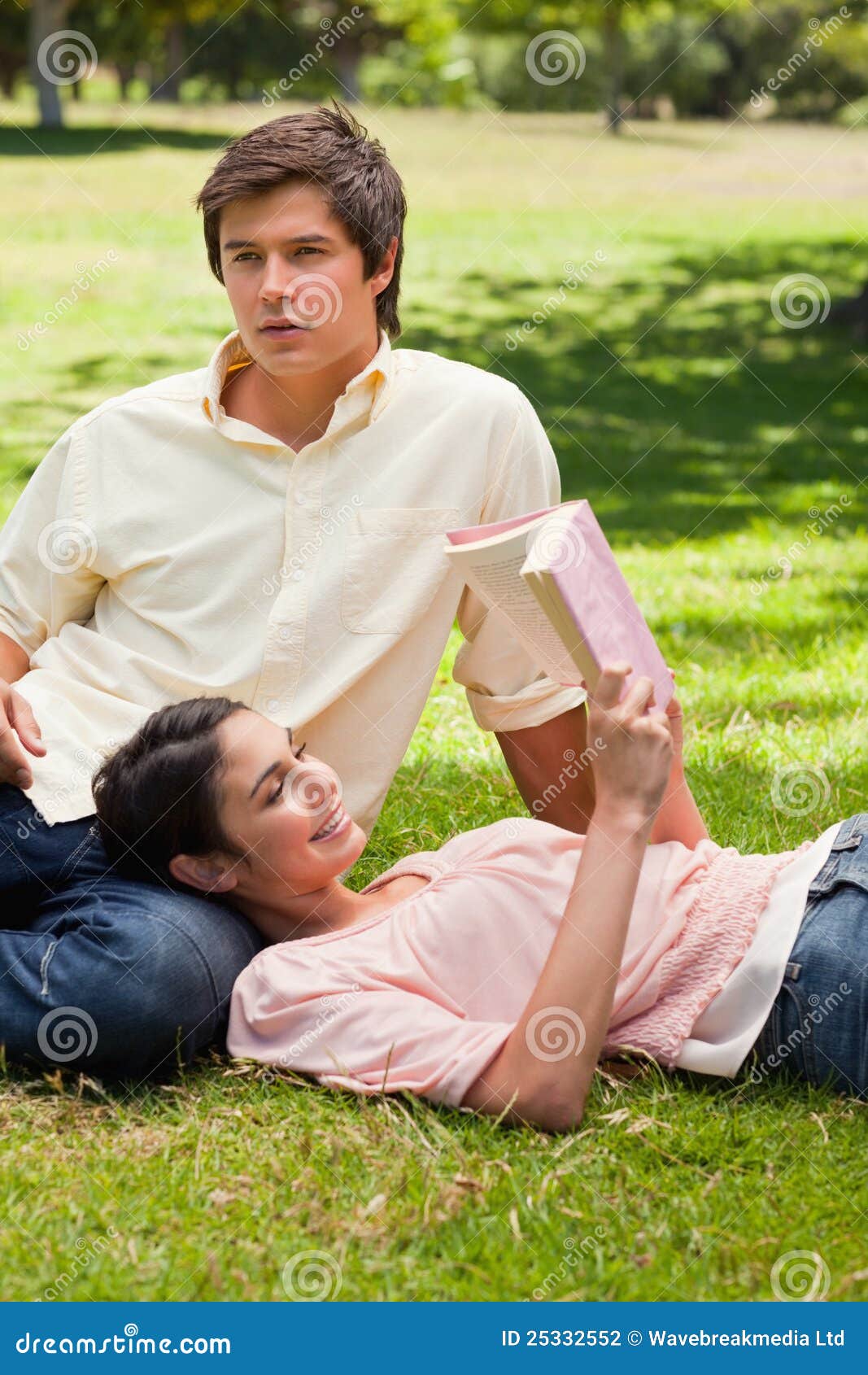Γυναίκα που βρίσκεται ενάντια στο πόδι του φίλου της ενώ διαβάζει. Γυναίκα που χαμογελά ενώ βρίσκεται ενάντια στο πόδι του φίλου της δεδομένου ότι διαβάζει ένα βιβλίο