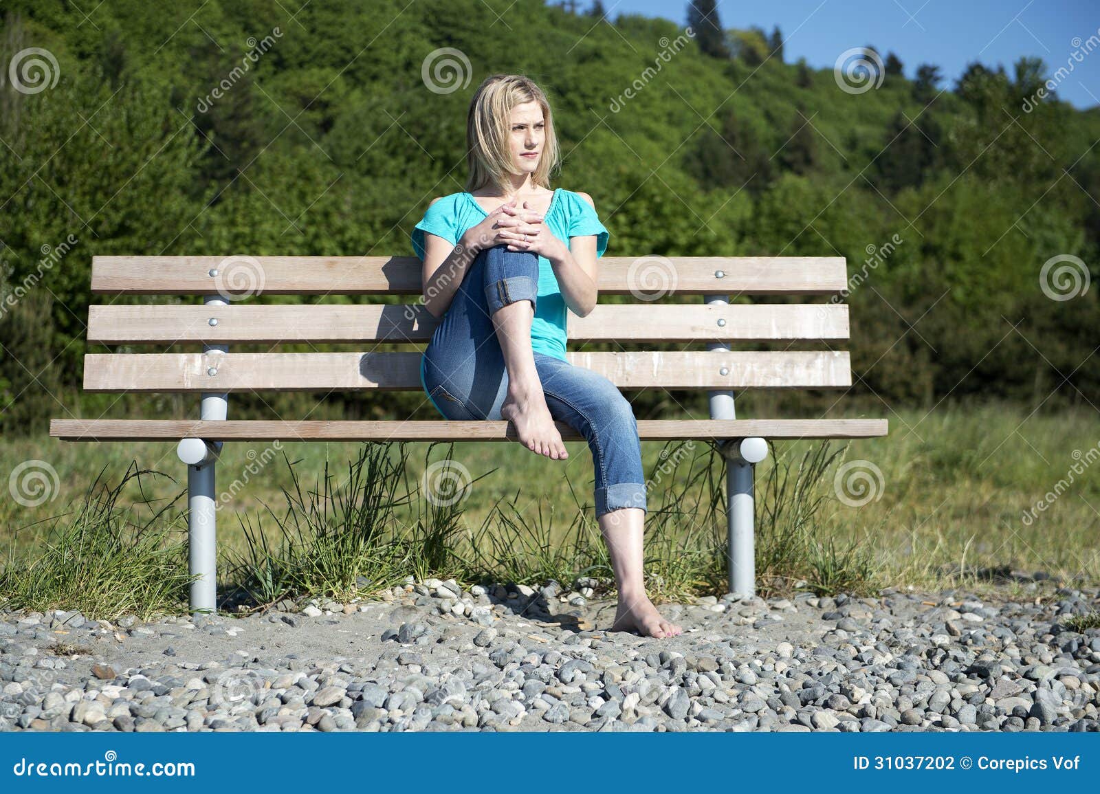 Γυναίκα στον πάγκο. Όμορφη γυναίκα, που κάθεται χωρίς παπούτσια σε έναν ξύλινο πάγκο στο πάρκο, ένα γόνατο που καταρτίζεται στο πρόσωπό της, που απολαμβάνει το θερμό φως του ήλιου άνοιξη