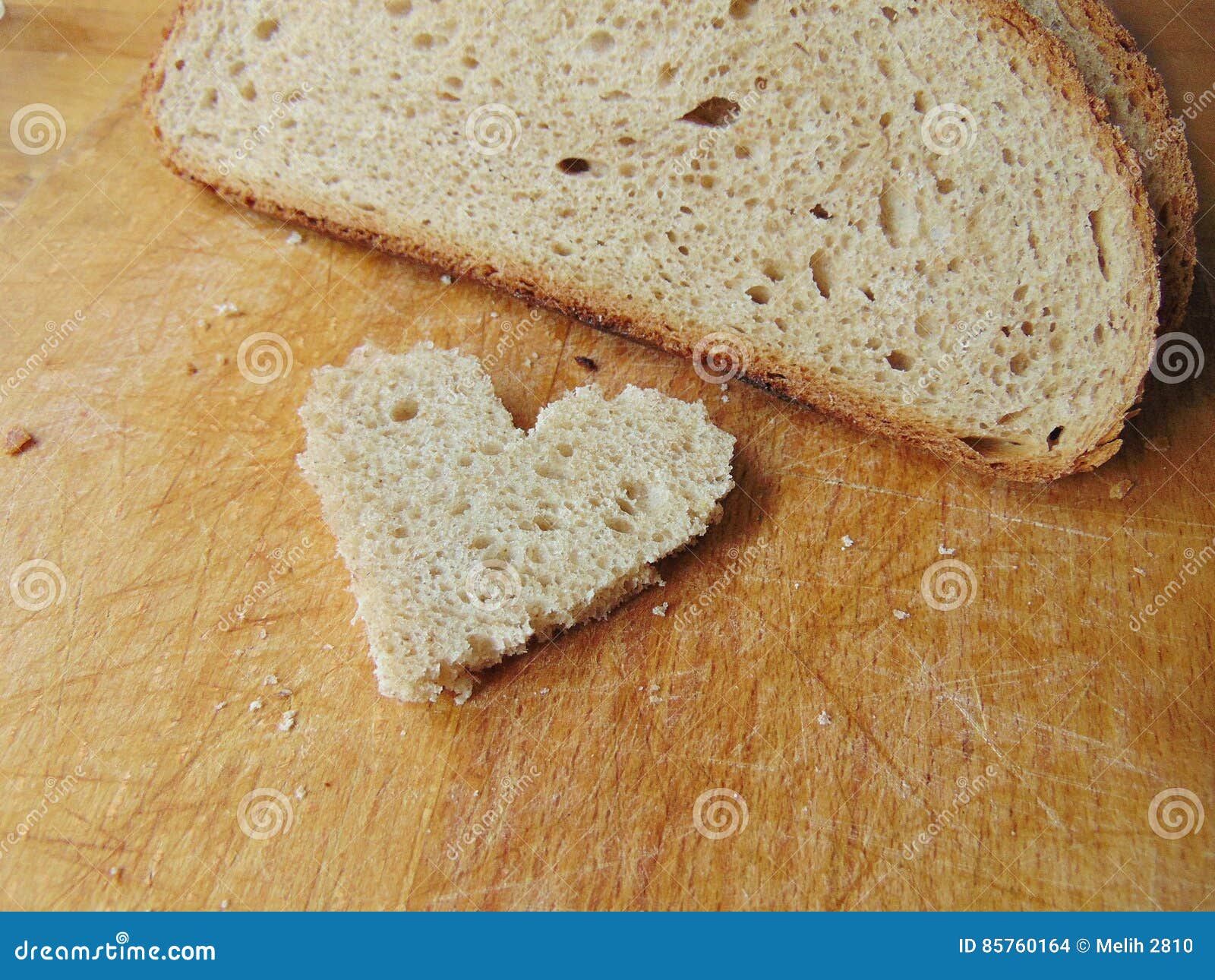 Διαμορφωμένο καρδιά κομμάτι του ψωμιού μπροστά από το πλήρες ψωμί. Η καρδιά διαμόρφωσε το κομμάτι του ψωμιού βάζοντας μπροστά από το πλήρες ψωμί στον ξύλινο τέμνοντα πίνακα