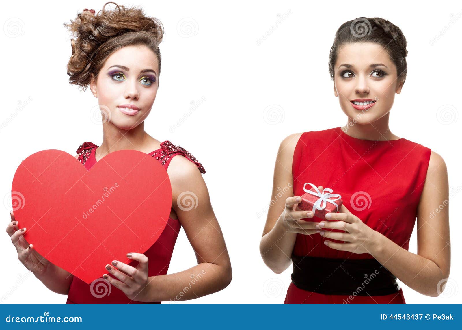Δύο νέες εύθυμες γυναίκες στο κόκκινο φόρεμα. Δύο νέες εύθυμες γυναίκες στην κόκκινα καρδιά και το δώρο εκμετάλλευσης φορεμάτων στο λευκό
