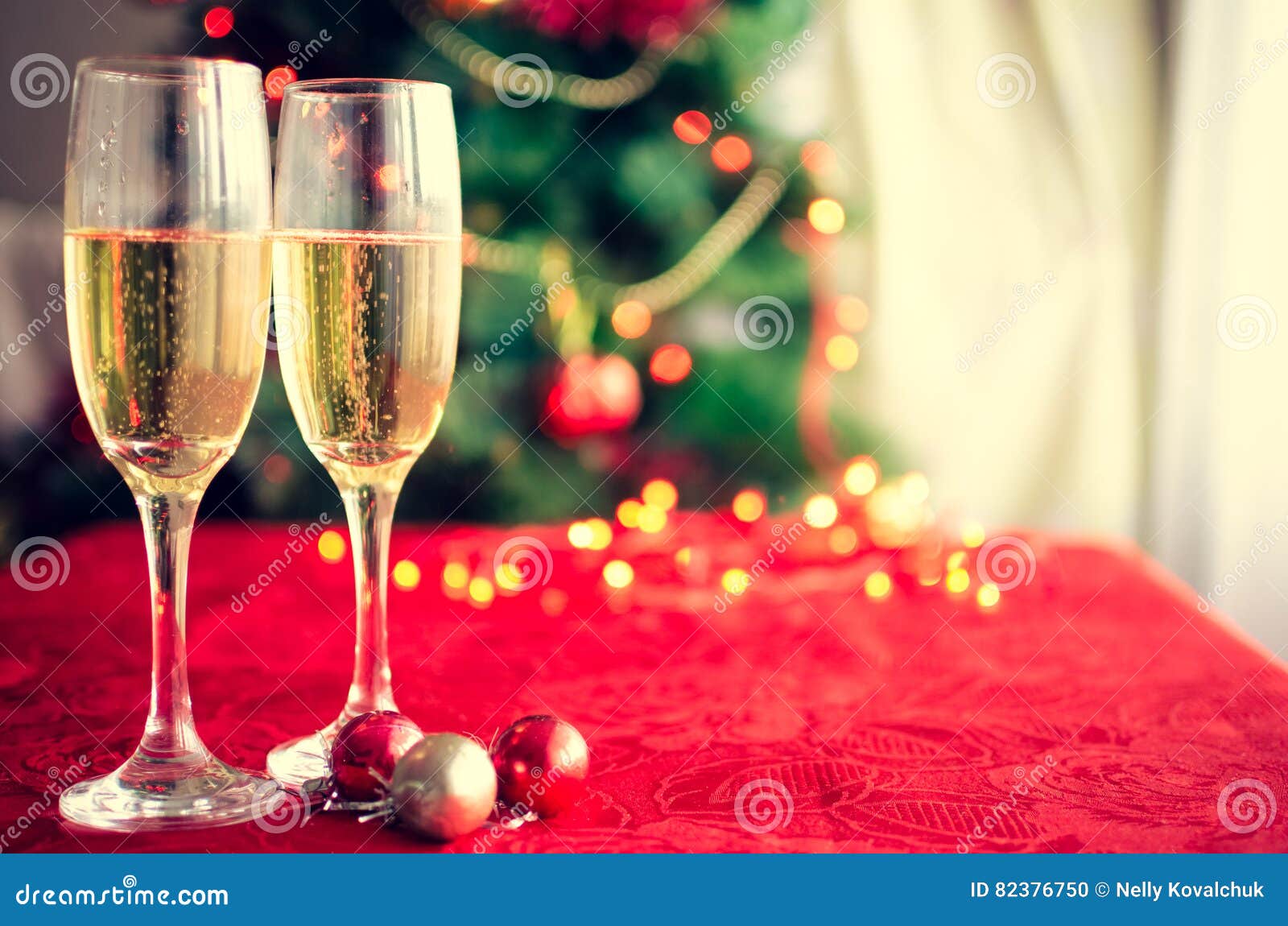 Δύο ποτήρια της σαμπάνιας κοντά στο όμορφο χριστουγεννιάτικο δέντρο Χύνοντας σαμπάνια στο γυαλί Χαρούμενα Χριστούγεννα και καλή χρονιά Ευμετάβλητο ύφος Εκλεκτική εστίαση