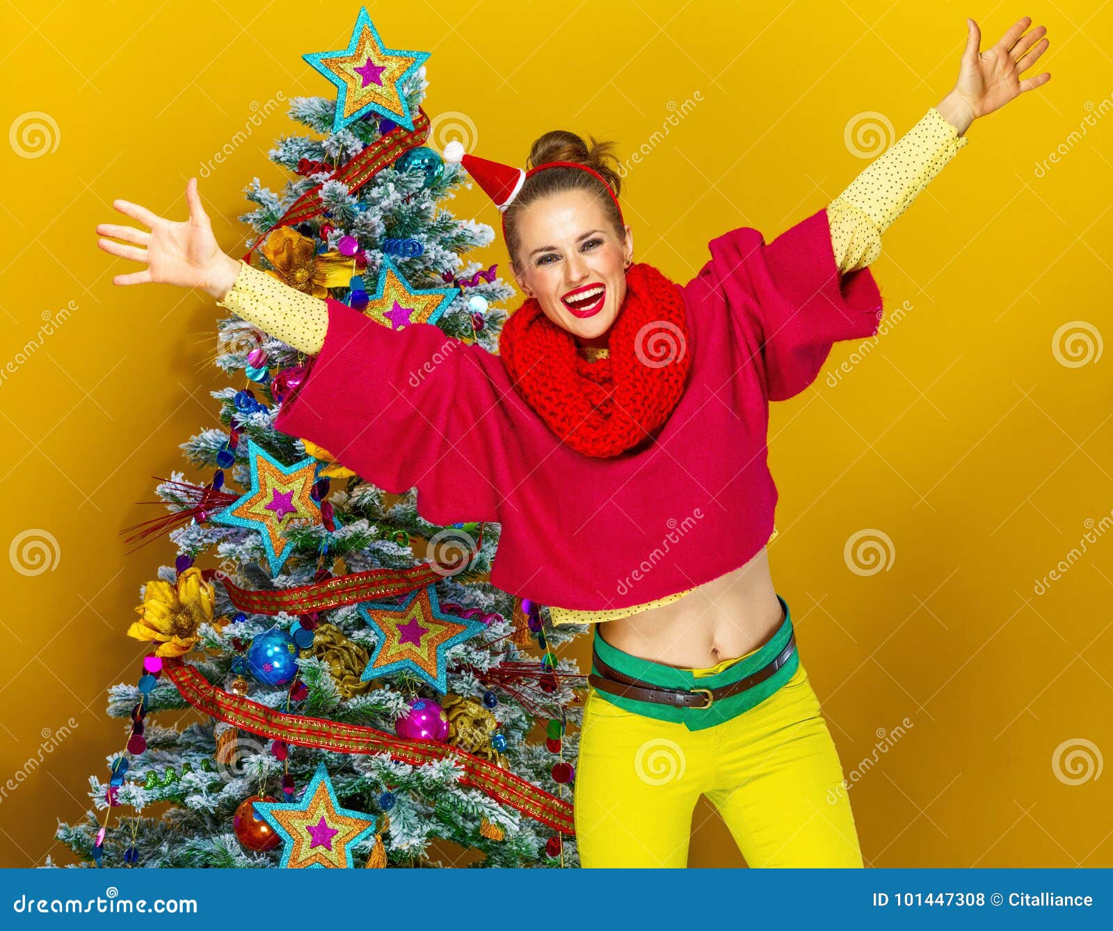 Ευτυχής γυναίκα κοντά στο χριστουγεννιάτικο δέντρο κίτρινο να χαρεί υποβάθρου. εορταστική εποχή ευτυχής νέα γυναίκα στα ζωηρόχρωμα ενδύματα κοντά στο χριστουγεννιάτικο δέντρο κίτρινο να χαρεί υποβάθρου