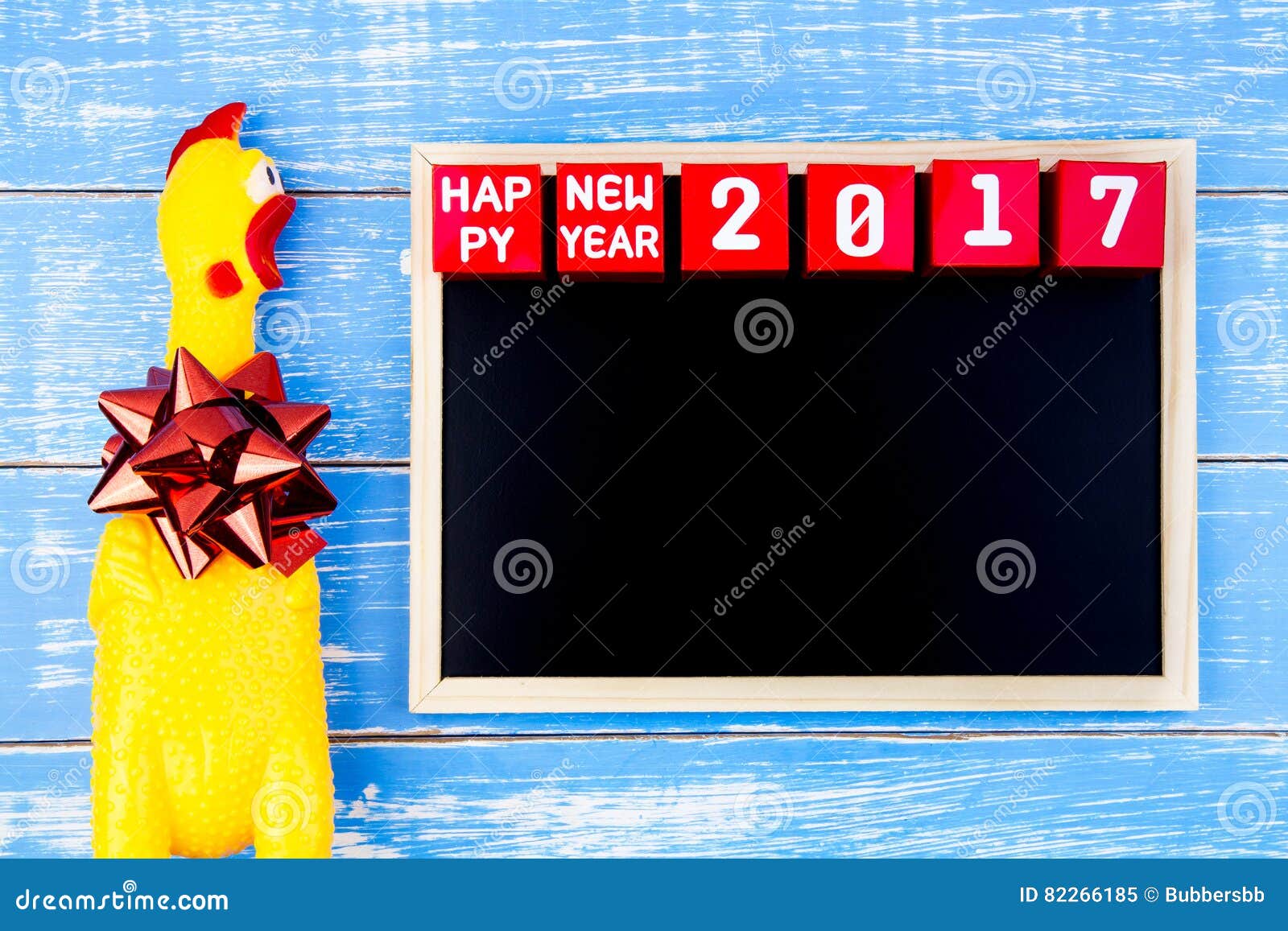 Κίτρινος κοτόπουλο παιχνιδιών, πίνακας και αριθμός καλής χρονιάς 2017 επάνω. Κίτρινος κοτόπουλο παιχνιδιών, πίνακας και αριθμός καλής χρονιάς 2017 στους κόκκινους κύβους κιβωτίων εγγράφου στο μπλε ξύλινο υπόβαθρο με το διάστημα αντιγράφων Έτος του κόκκορα 2017 νέο υπόβαθρο έννοιας έτους