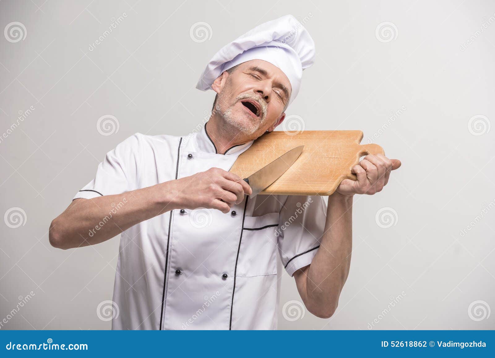 ο κύριος μάγειρας απομόνωσε το λευκό. Ανώτερος αρσενικός κύριος μάγειρας στο ομοιόμορφο μαχαίρι εκμετάλλευσης και τεμαχίζοντας πίνακας α στο γκρίζο υπόβαθρο