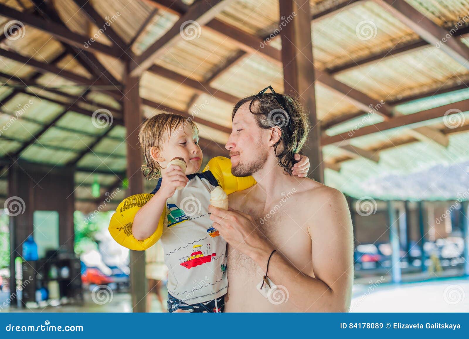 Ο πατέρας και ο γιος που τρώνε το παγωτό στο aquapark κάτω από το α η στέγη. Ο πατέρας και ο γιος που τρώνε το παγωτό στο aquapark κάτω από το α η έννοια διακοπών στεγών
