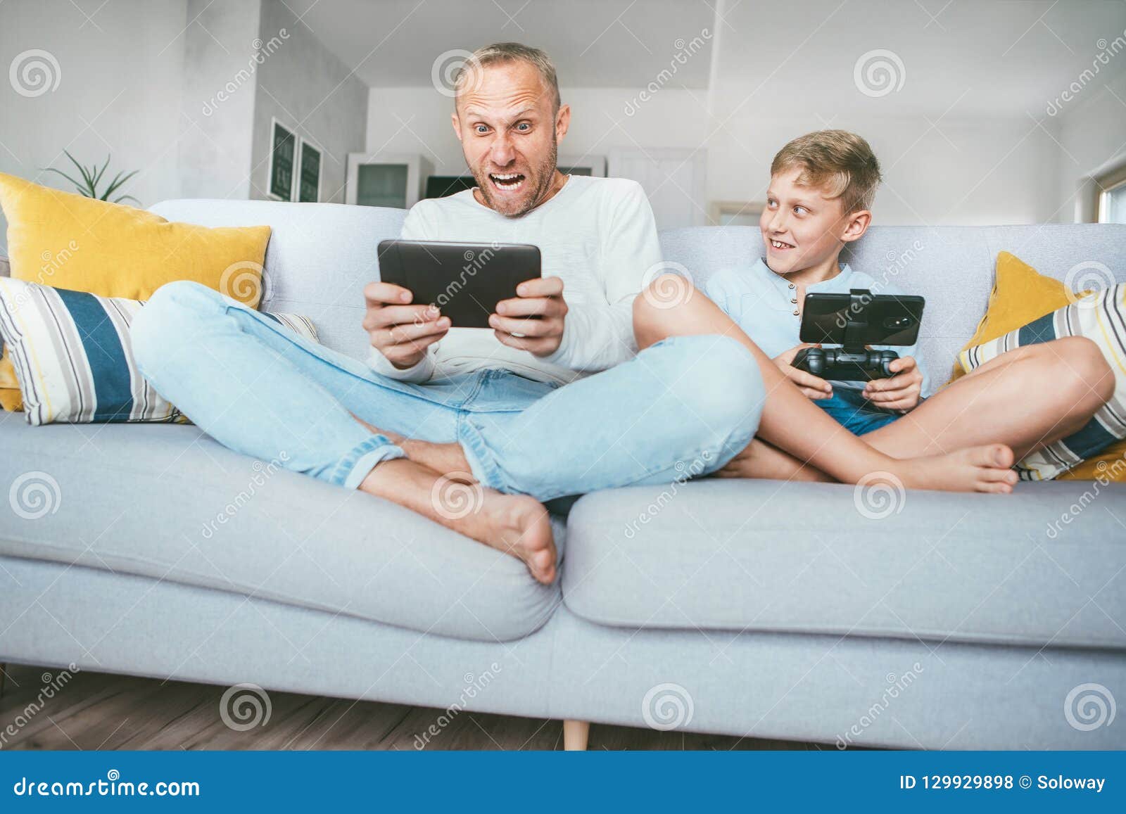 Ο πατέρας μου funs από τα παιχνίδια PC ακριβώς όπως με Πατέρας και γιος που παίζουν συναισθηματικά με τις ηλεκτρονικές συσκευές: ταμπλέτα και gamepad συνεδρίαση στο καθιστικό