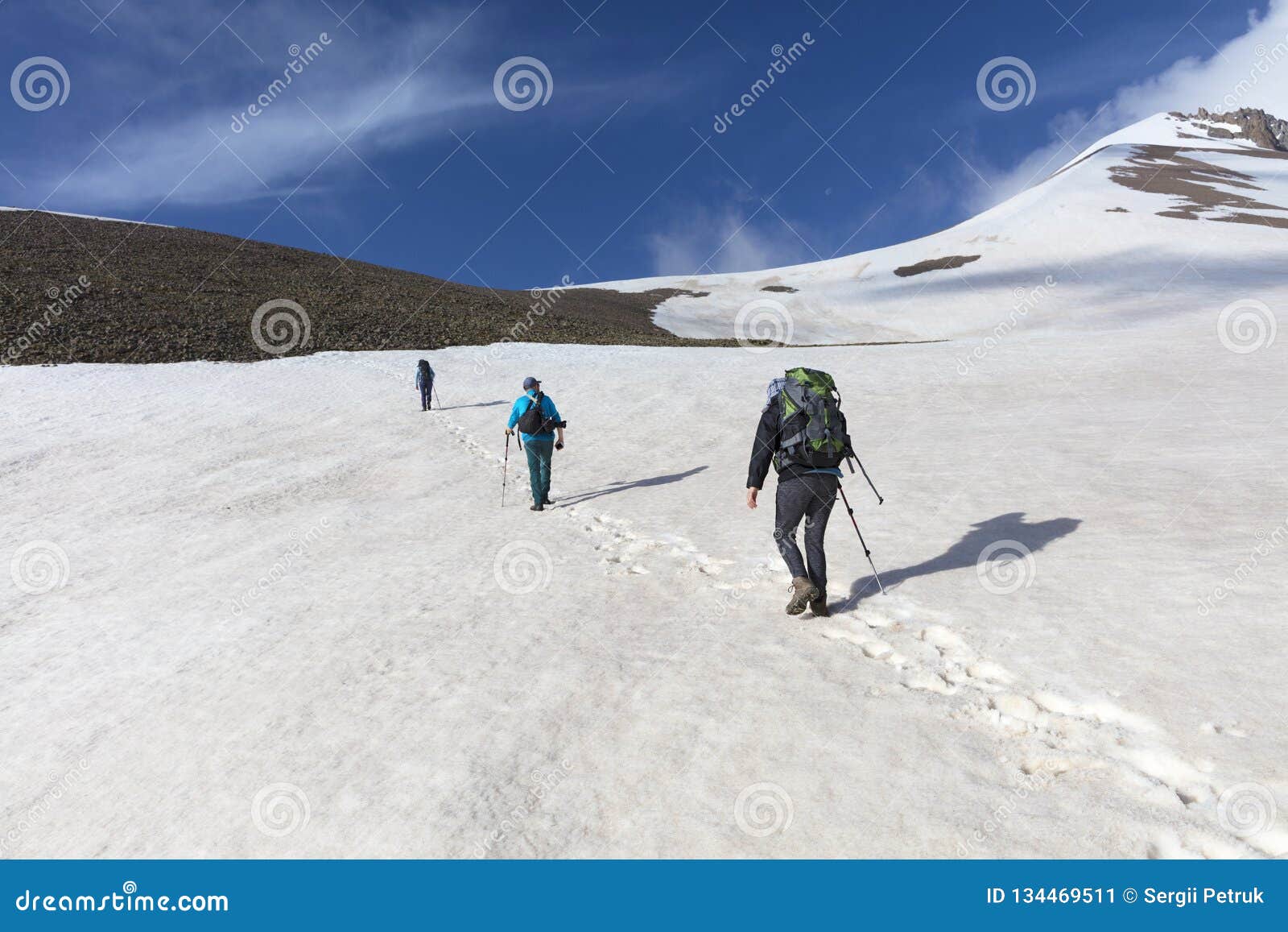 Οι τουρίστες ανέρχονται επάνω mountainside στη χιονοσκεπή σύνοδο κορυφής. Μια ομάδα τουριστών με τα σακίδια πλάτης πηγαίνει σε ένα χιονώδες βουνό