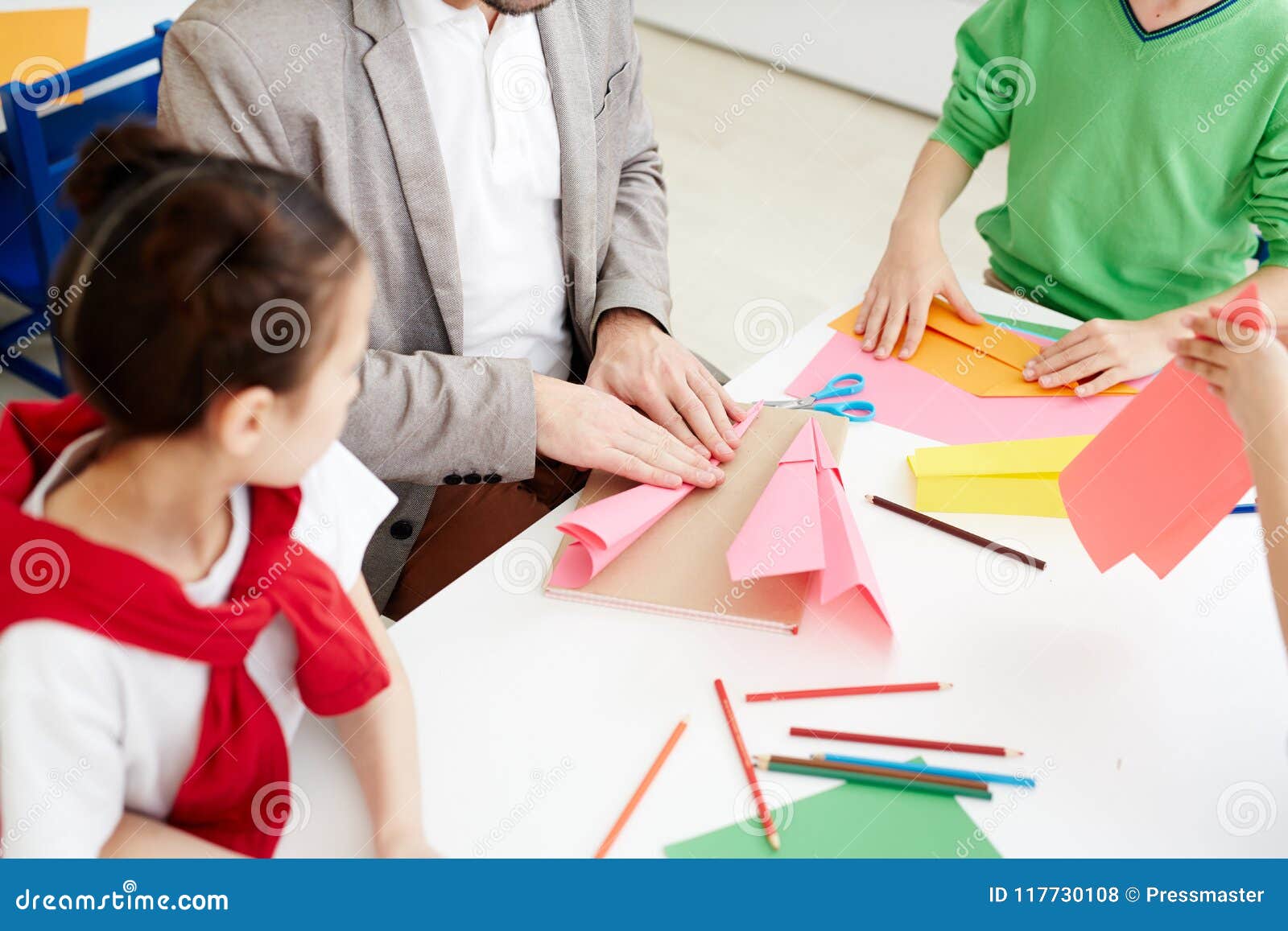 Παιδιά που κατασκευάζουν τα αεροπλάνα εγγράφου με το χρωματισμένο έγγραφο κατά τη διάρκεια του μαθήματος τέχνης καθμένος στο γραφείο τάξεων με το δάσκαλο