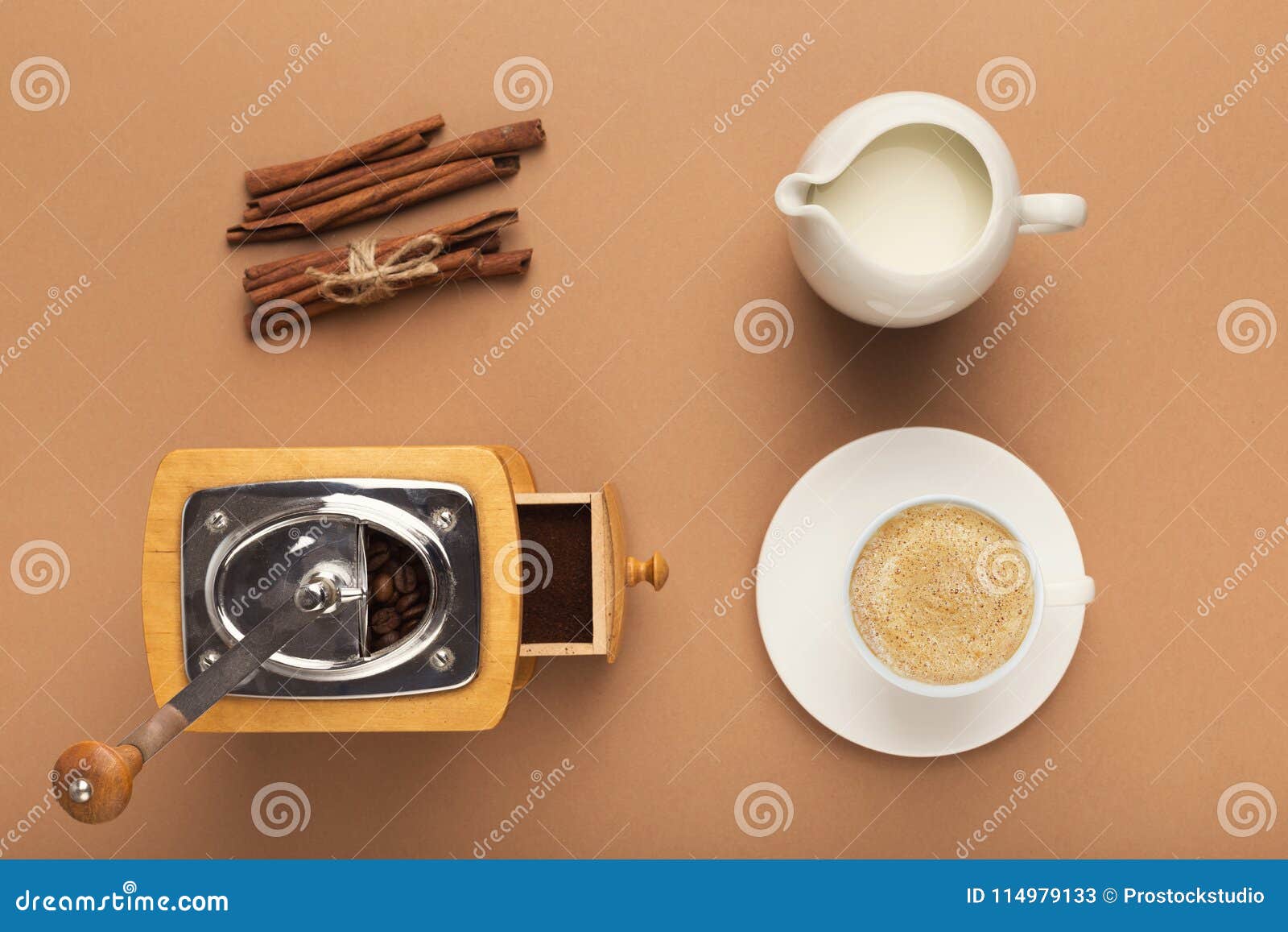 Προετοιμασία του υποβάθρου καφέ, τοπ άποψη. Τοπ άποψη σχετικά με τον εκλεκτής ποιότητας μύλο καφέ, το βάζο γάλακτος, το φλυτζάνι και την κανέλα στο μπεζ σκηνικό Παραγωγή του foamy υποβάθρου cappuccino, διάστημα αντιγράφων