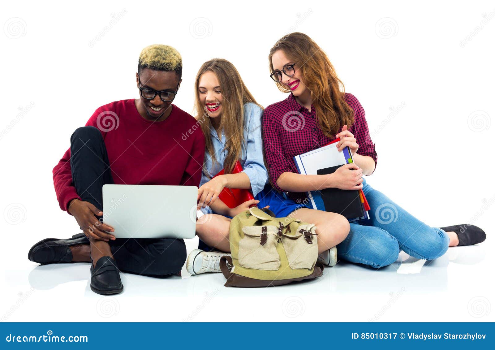 Τρεις ευτυχείς σπουδαστές που κάθονται με τα βιβλία, το lap-top και τις τσάντες