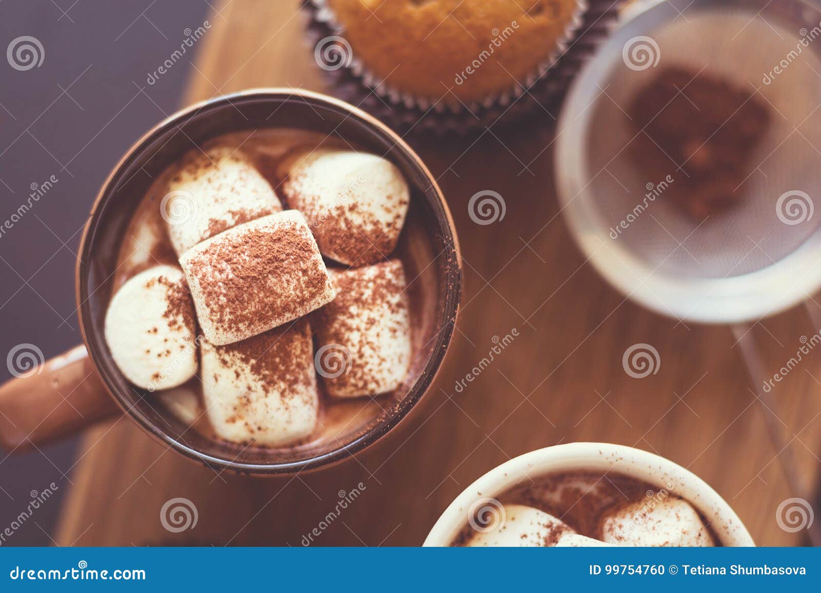 Φλυτζάνια με την καυτή σοκολάτα με marshmallow και muffins στο σκοτεινό ξύλινο γραφείο Εκλεκτική εστίαση εικόνα που τονίζεται