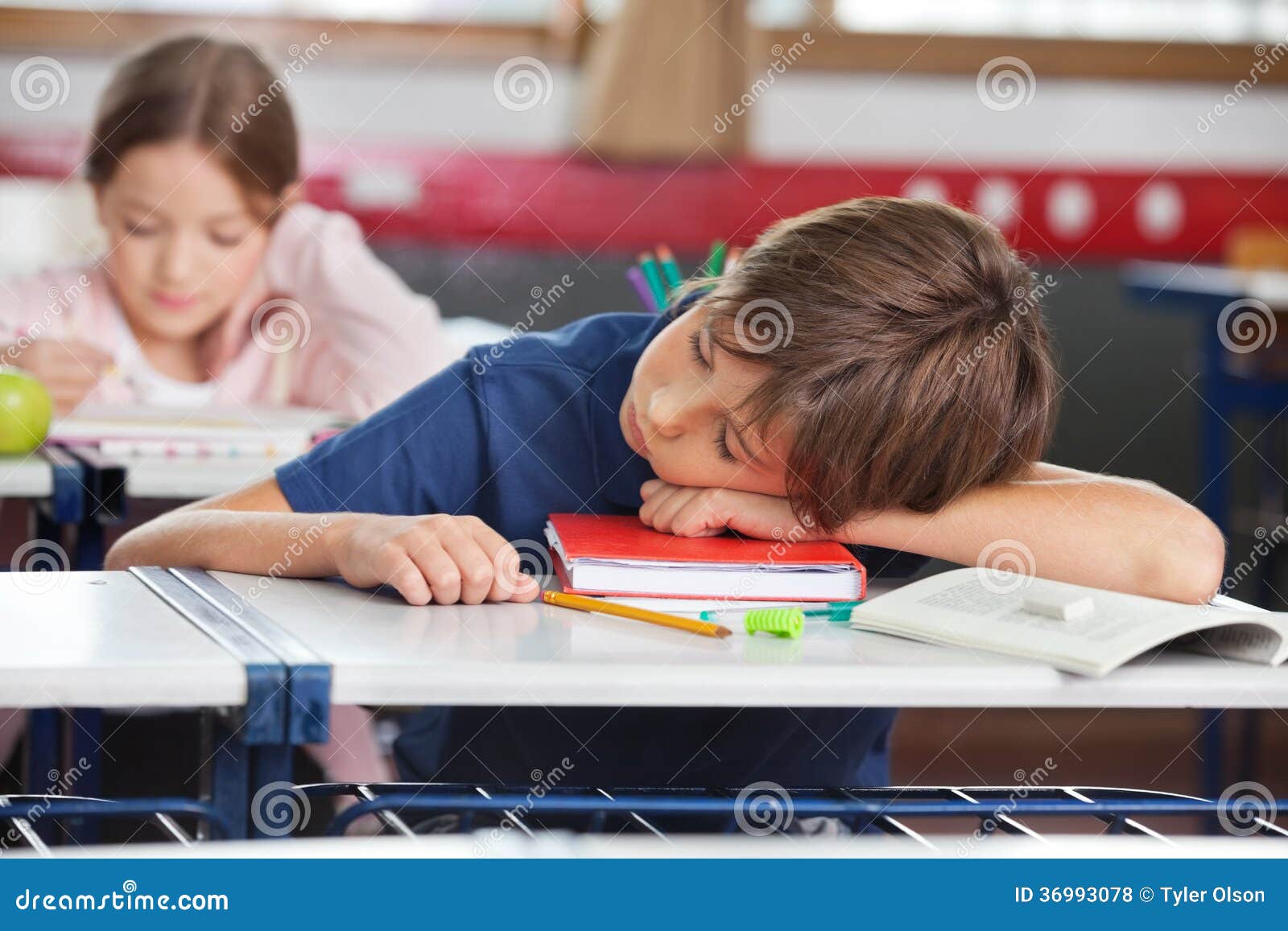 Ύπνος αγοριών ενώ κορίτσι που μελετά στο υπόβαθρο. Στοιχειώδης ύπνος αγοριών ενώ κορίτσι που μελετά στο υπόβαθρο στην τάξη