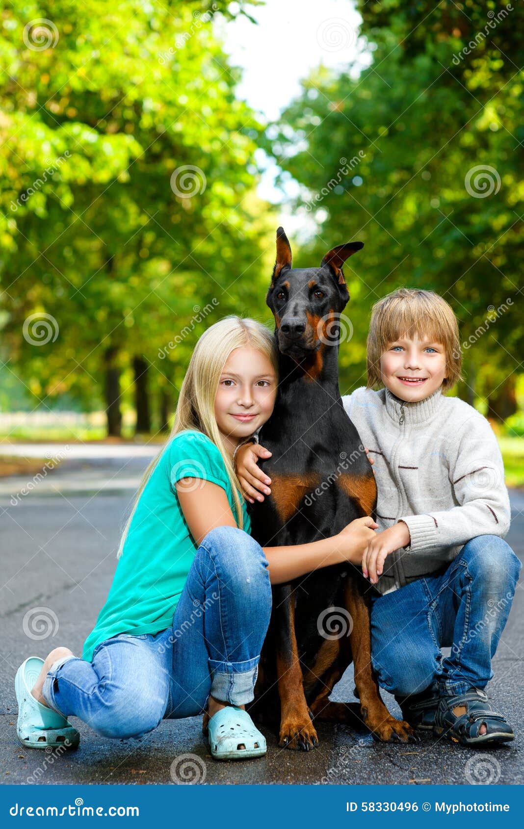 Белокурые объятия любимая собака или doberman девушки и мальчика в парке лета