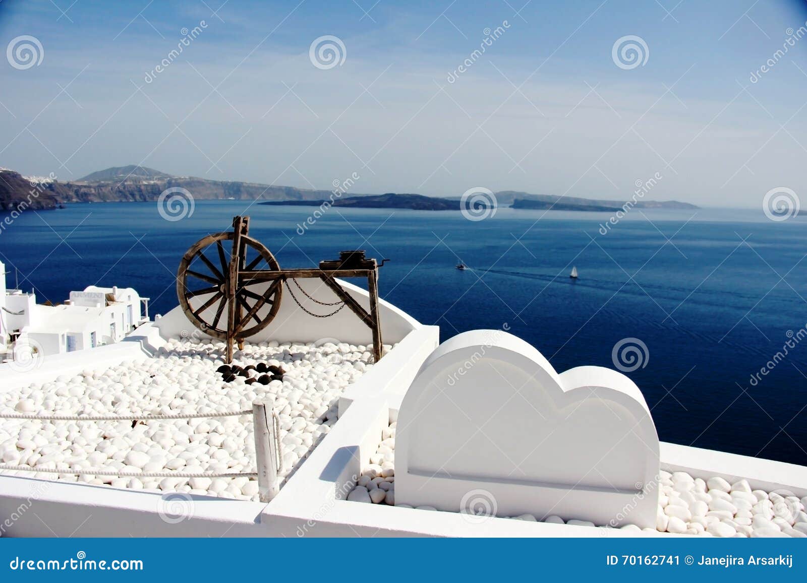 Белые украшения на белых зданиях, Santorini, Греции. Катите на холм, белые здания, с предпосылкой голубого Эгейского моря и голубого неба в Santorini, Греция
