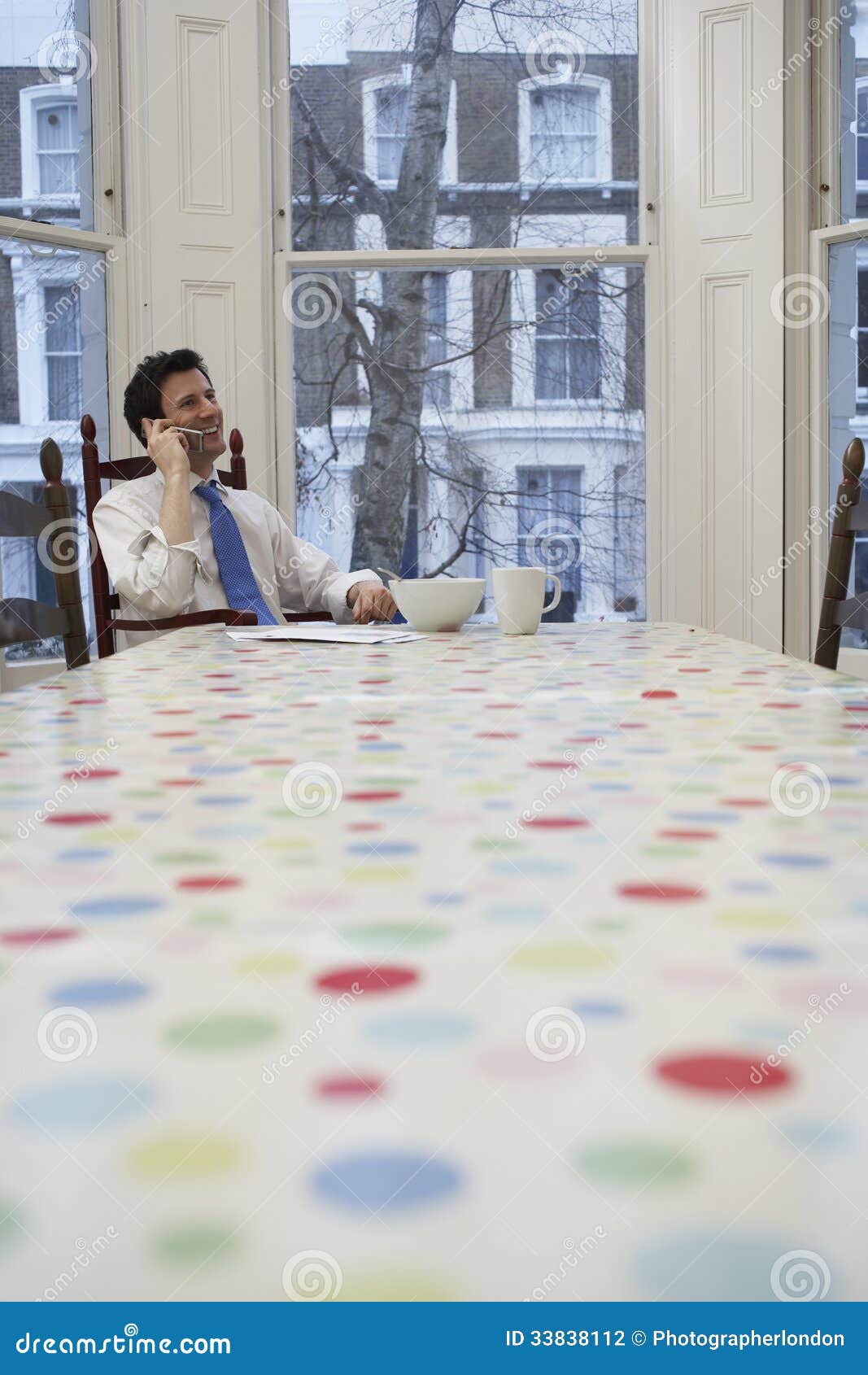 Бизнесмен используя мобильный телефон на обеденном столе. Молодой бизнесмен в formals используя мобильный телефон на обеденном столе