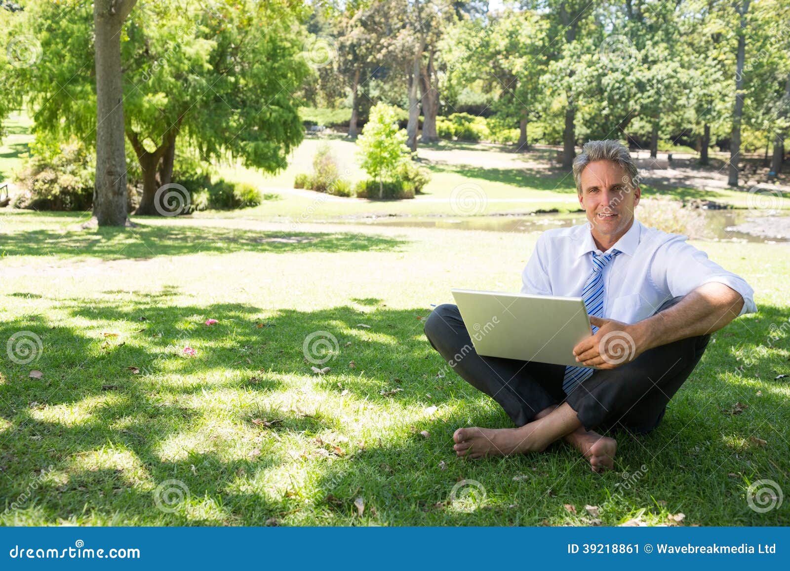 бизнесмен при компьтер-книжка сидя на траве. Полнометражный портрет зрелого бизнесмена при компьтер-книжка сидя на траве в парке