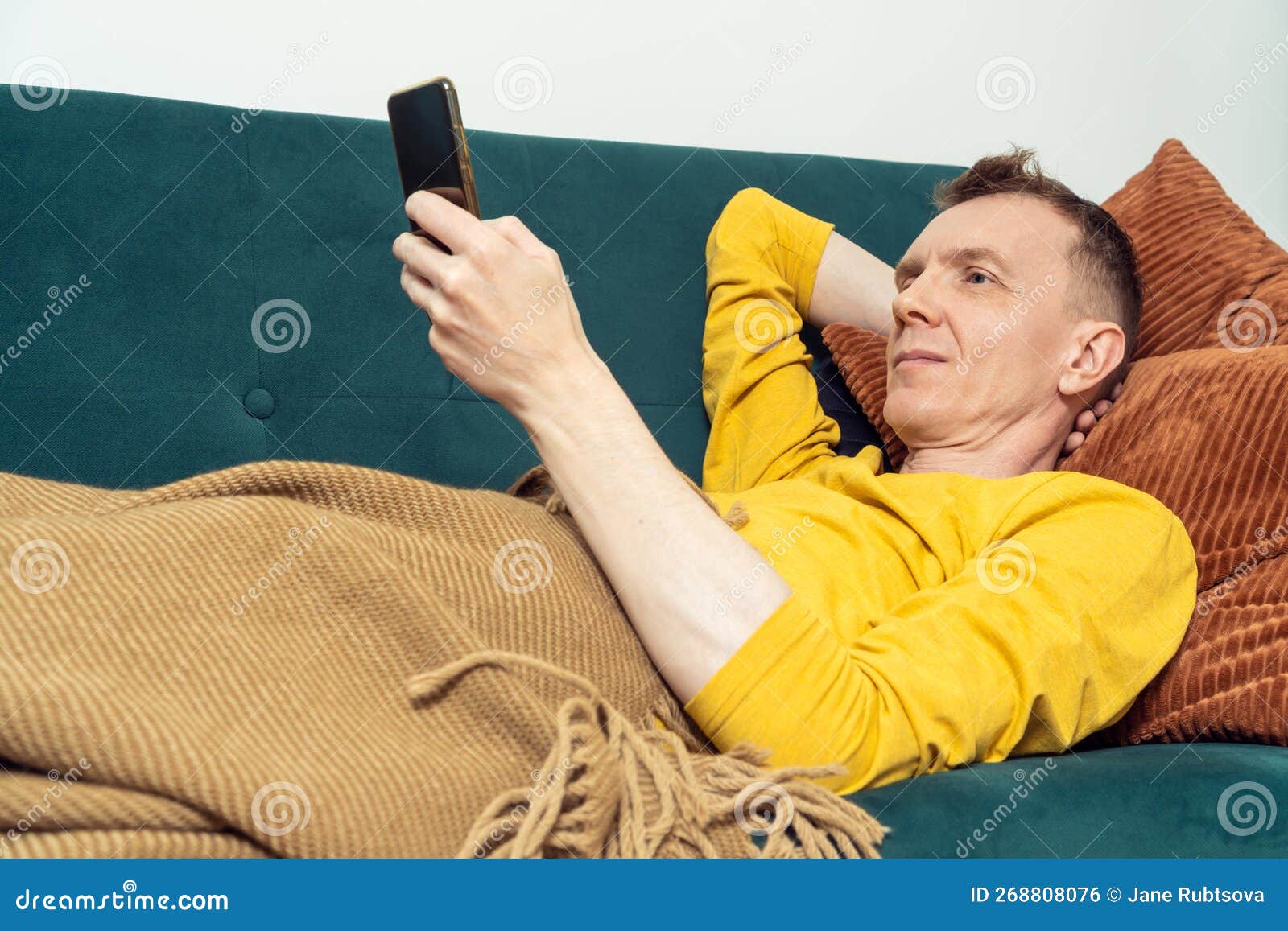 Мужчина с гриппом лежит на диване и сморкается