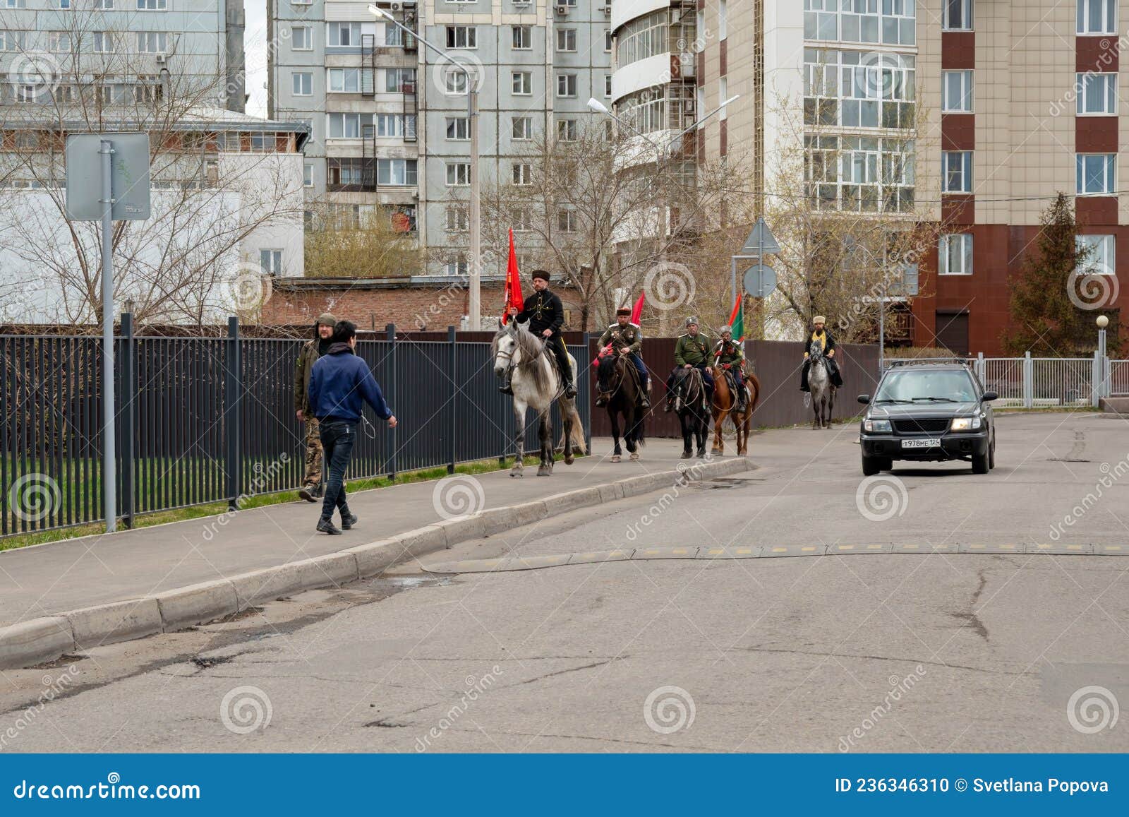 группа казаков с флагами на лошади вдоль тротуара на фоне жилых зданий ...