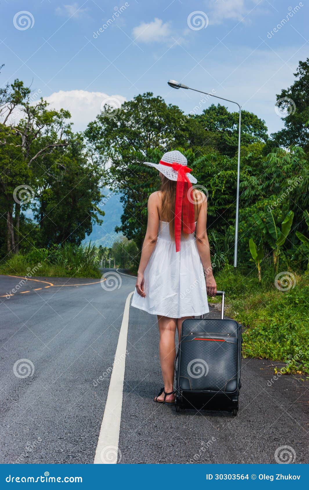 Девушка с чемоданом на дезертированной дороге в одичалых джунглях