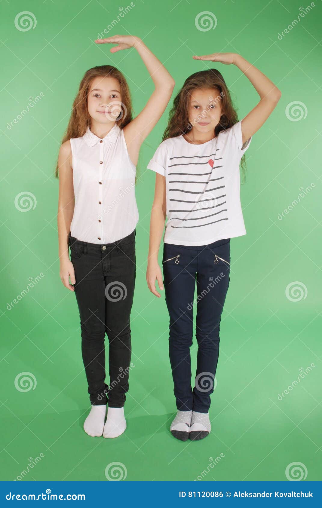 2 девушки школы держат руки над головой и измерять его рост изолированные на зеленом цвете