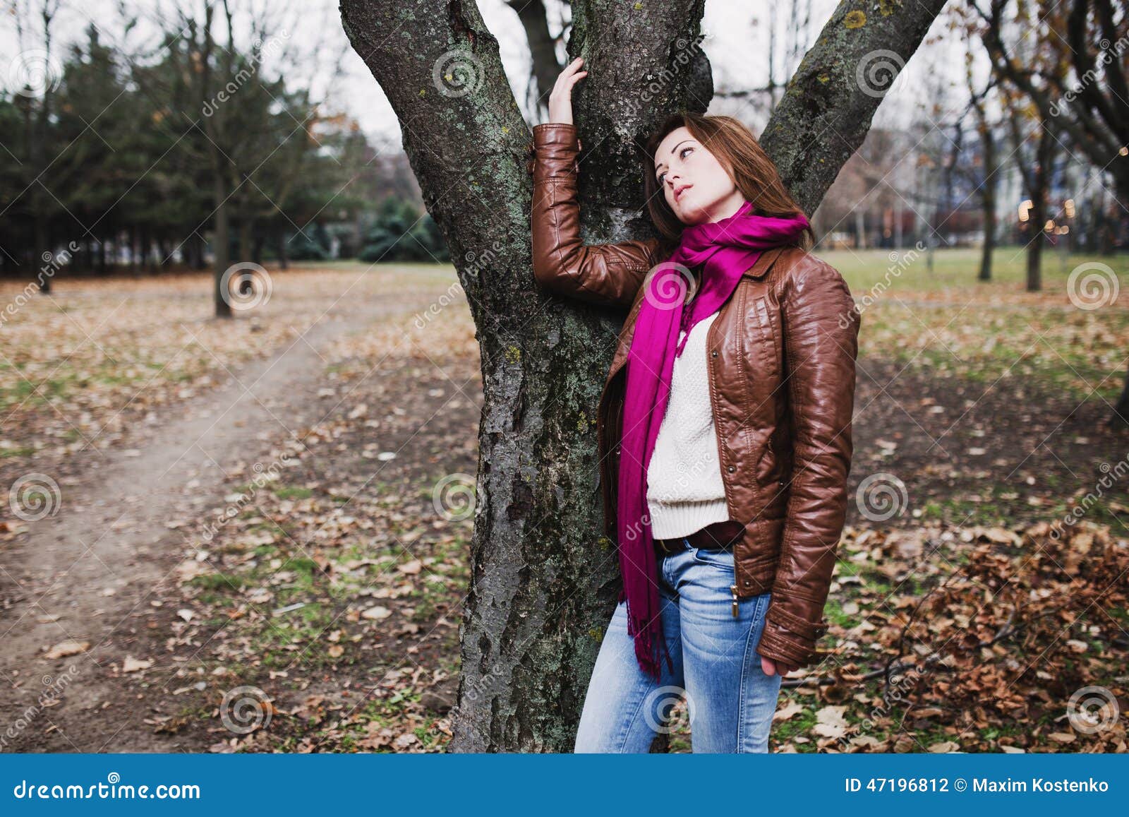 Задумчивая молодая девушка брюнет стоя близко дерево в парке осени
