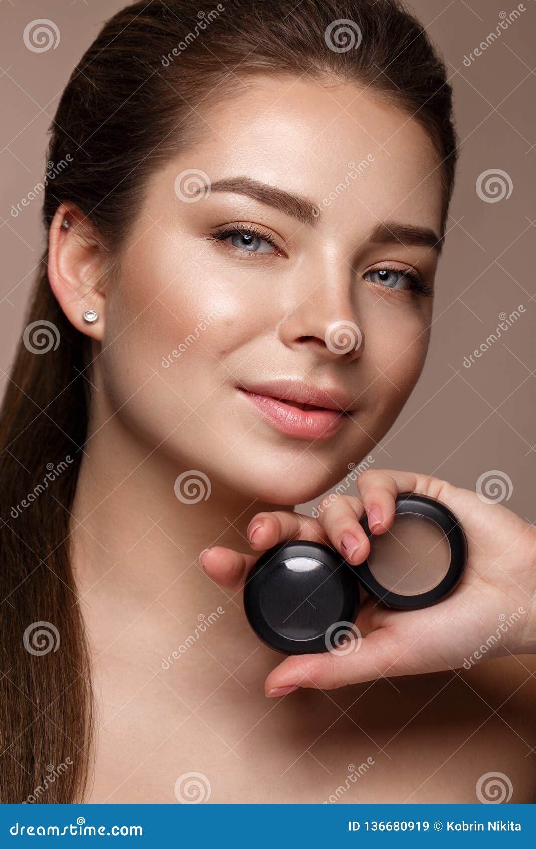 Красивая маленькая девочка с естественным обнаженным макияжем с косметикой в руках Сторона красотки Фото принятое в студию