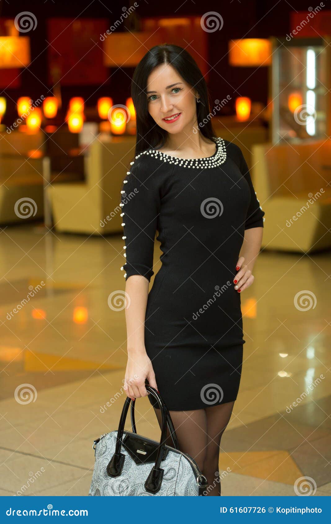 Красивая молодая женщина в роскошном красном платье представляя с хозяйственными сумками в моле на предпосылке окон магазина серия