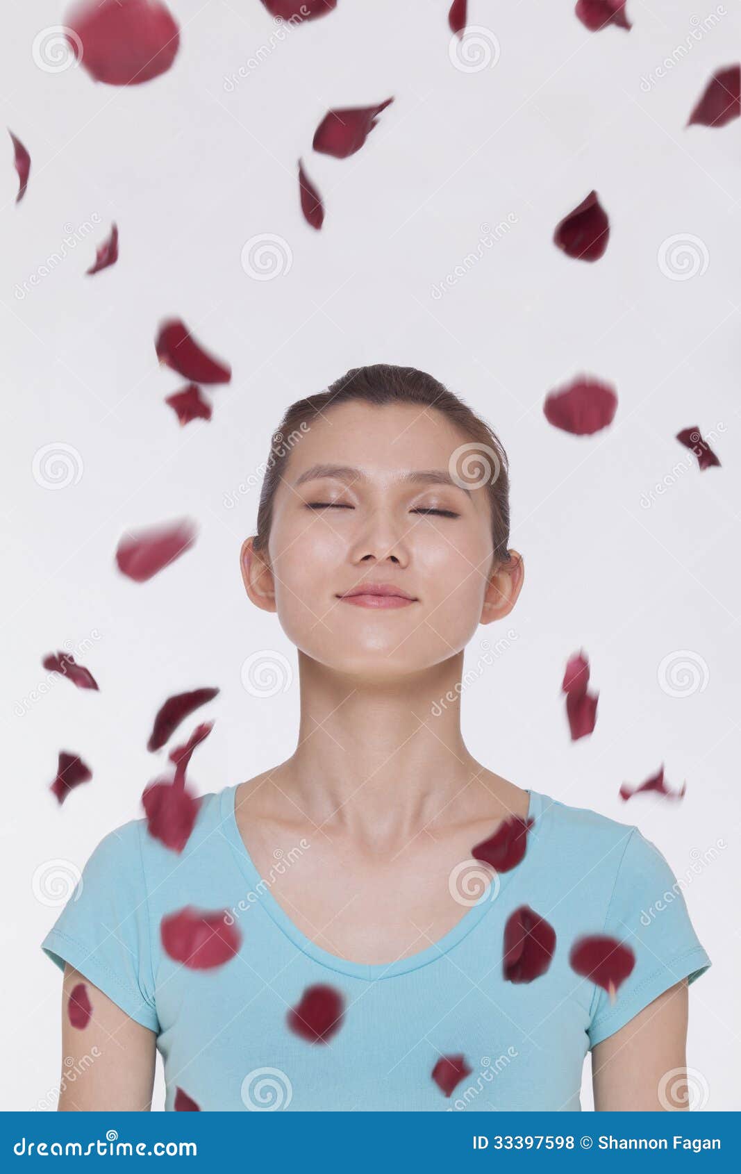 Красивая спокойная молодая женщина смотря вверх с глазами закрыла при лепестки розы летая вокруг ее