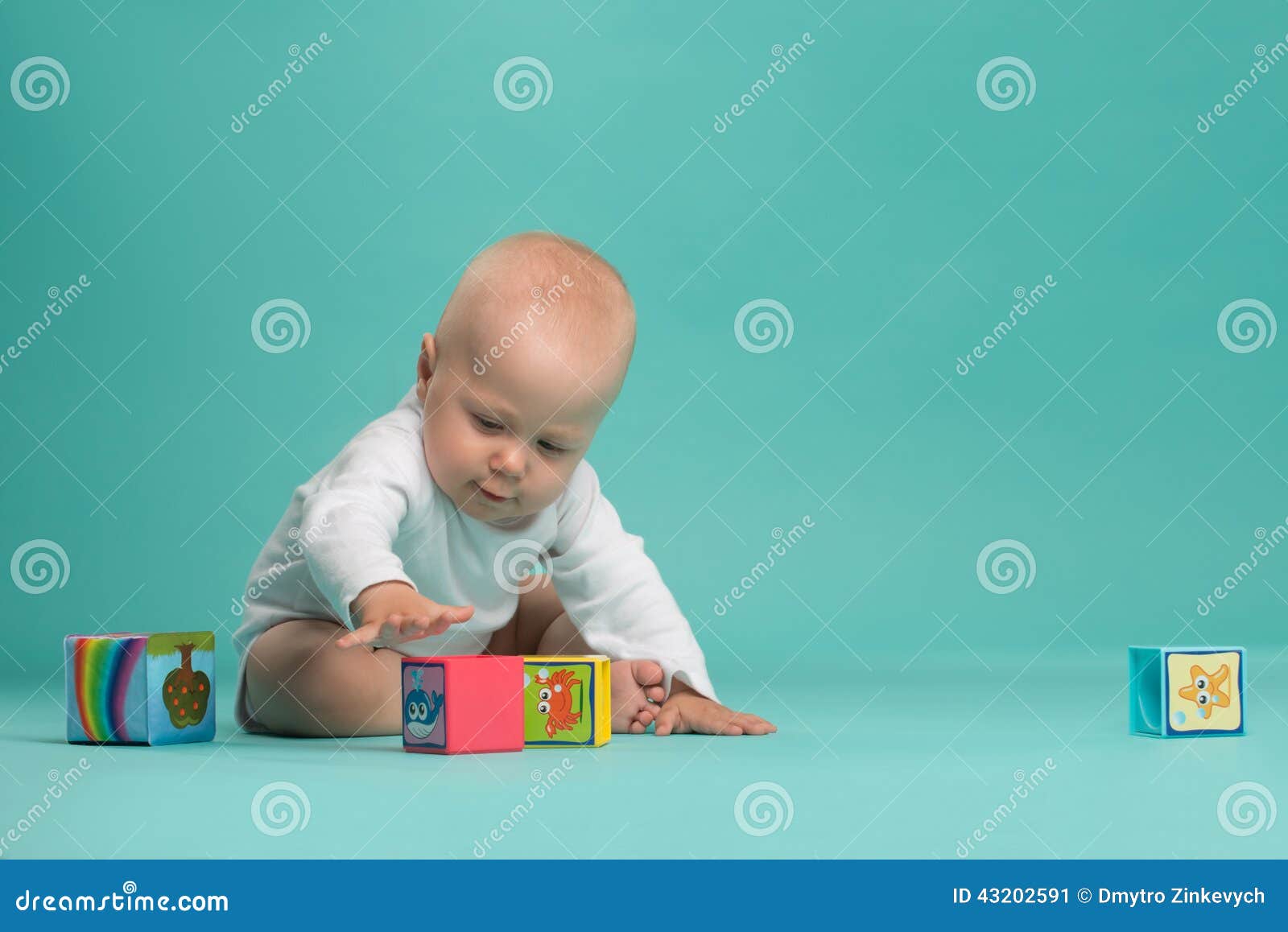 Маленький милый ребёнок играя с блоками цвета. Bodysuit маленького милого ребёнка нося белый играя при покрашенные блоки, изолированные на сини