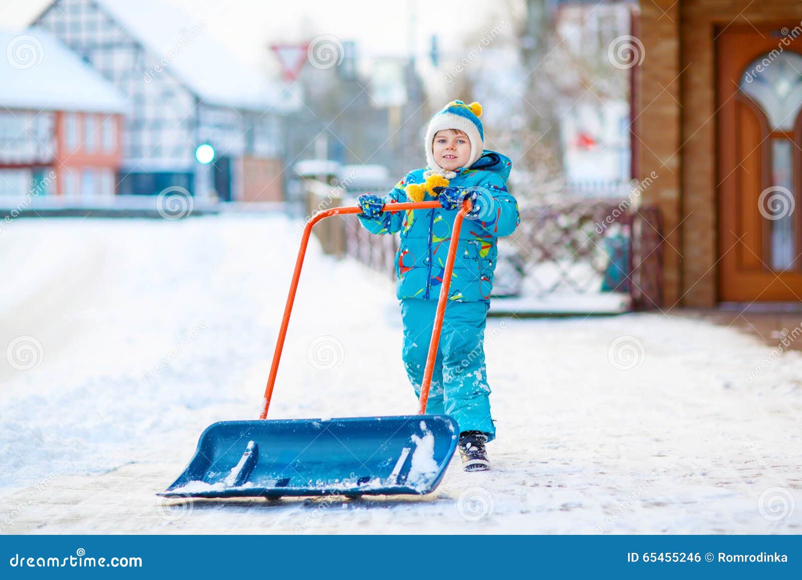 Мальчик маленького ребенка играя с снегом в зиме. Милый мальчик маленького ребенка в красочных одеждах зимы имея потеху с лопаткоулавливателем снега, outdoors во время снежностей Active отдых outdoors с детьми в зиме Счастливый ребенок с теплой шляпой, перчатками, модой зимы